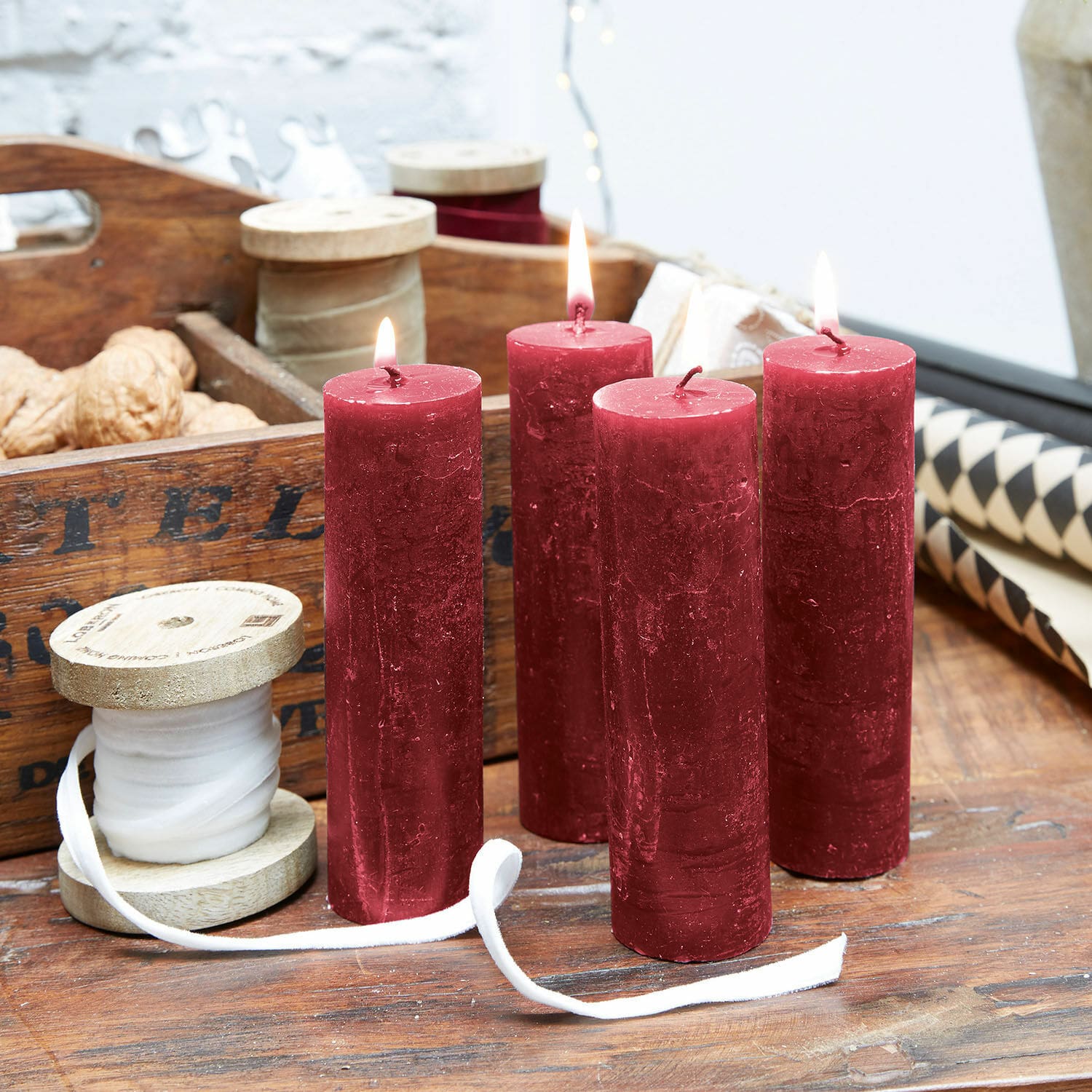 Set di 4 candele Muriel Quattro candele rosse in cera su tavolo di legno con rocchetti decorativi e noci