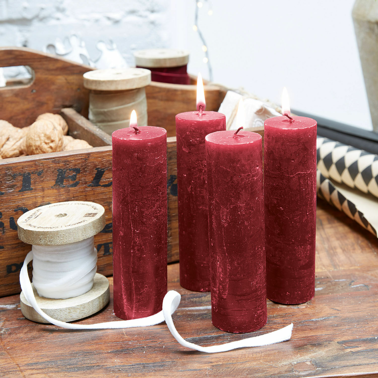 Set di 4 candele Muriel Quattro candele rosse in cera su tavolo di legno con rocchetti decorativi e noci