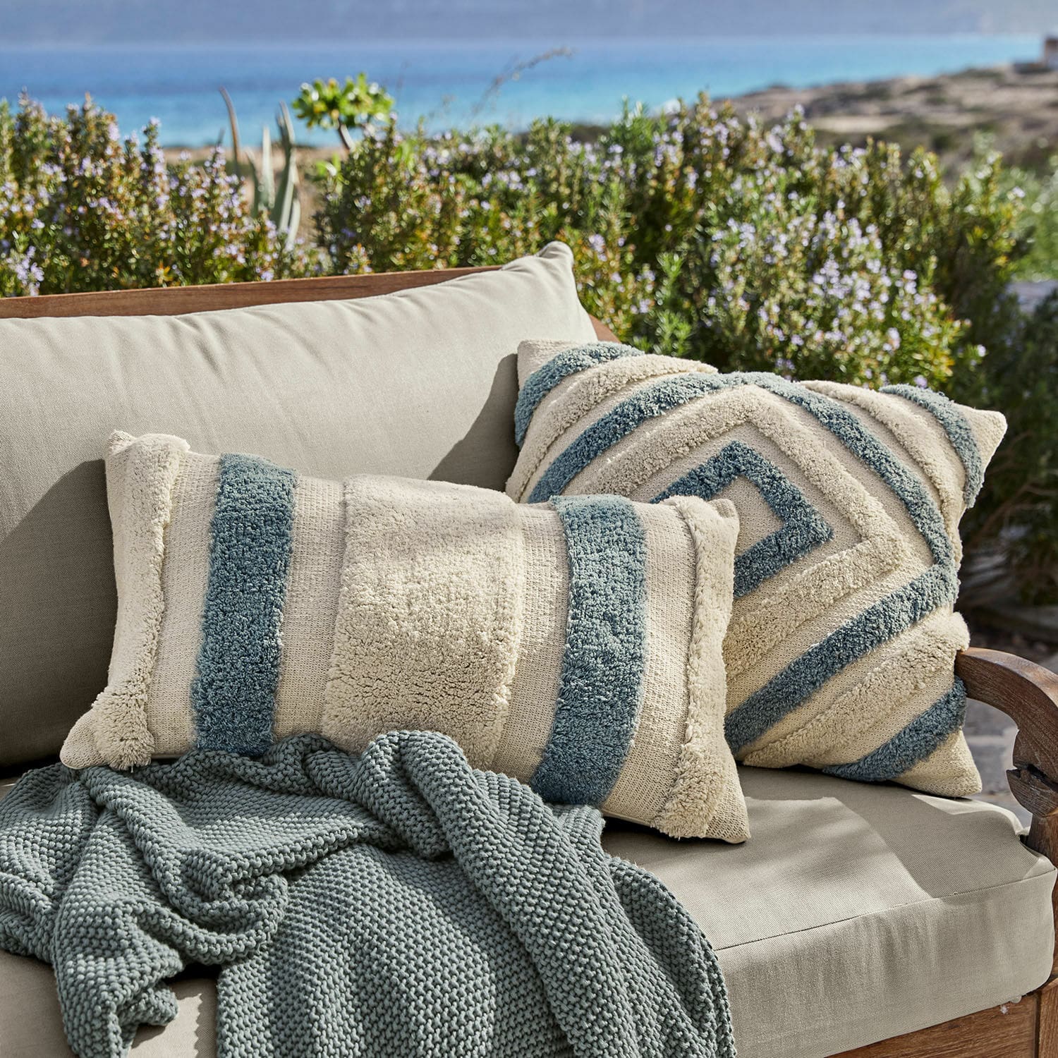 Coppia di copricuscini Melyn Cuscini decorativi beige e blu in materiale morbido su divano beige con coperta lavorata a maglia