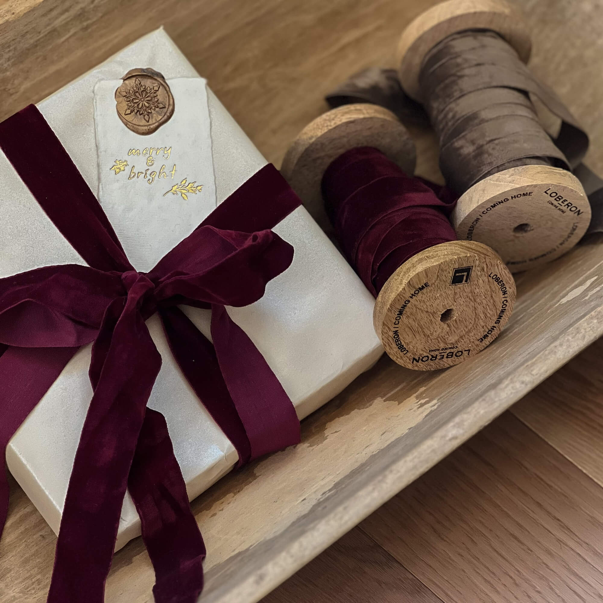 Regalo avvolto in carta bianca con nastro di velluto bordeaux e bobine di legno con nastri decorativi