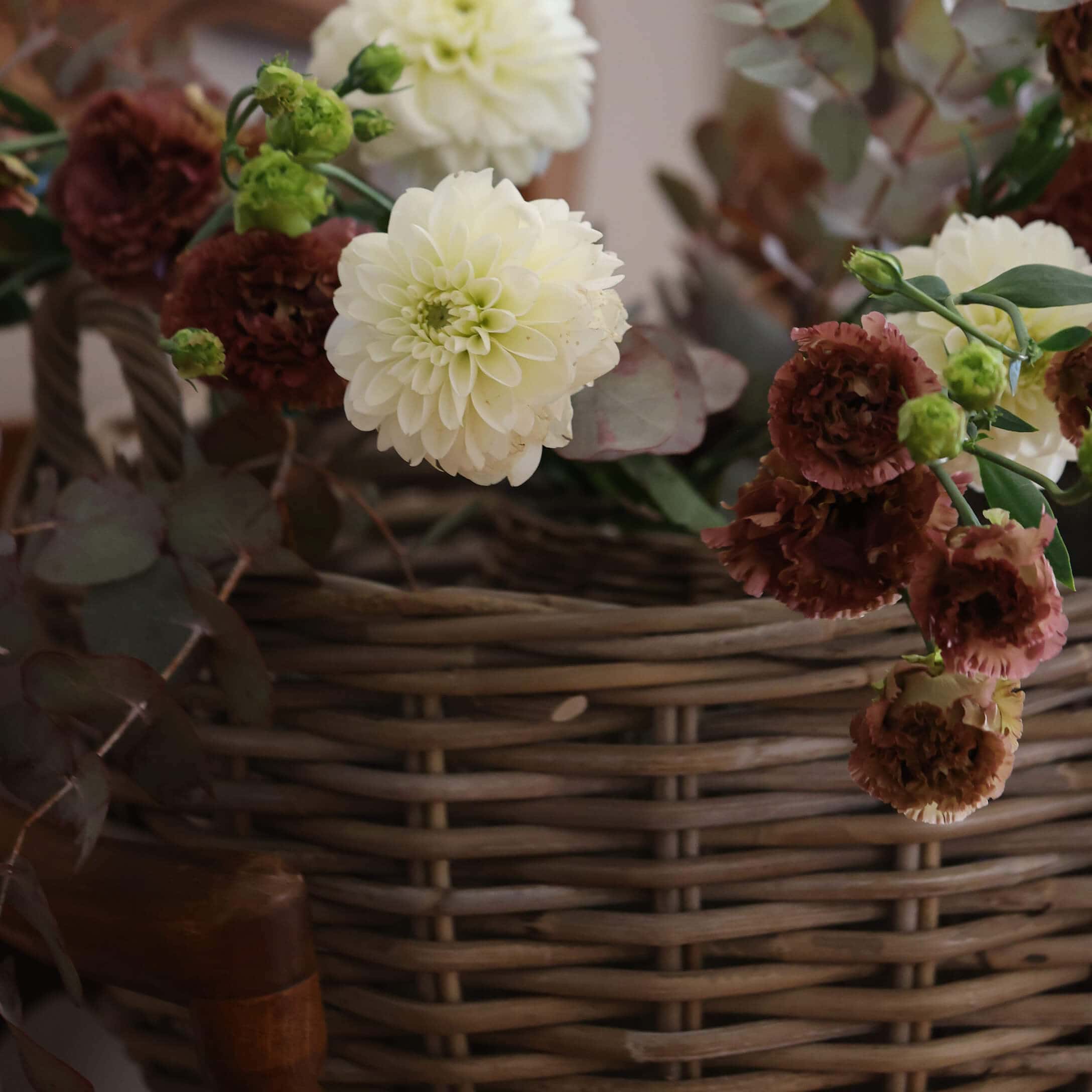 Mazetto di fiori crema e bordeaux in cesto di vimini per decorazione d'interni