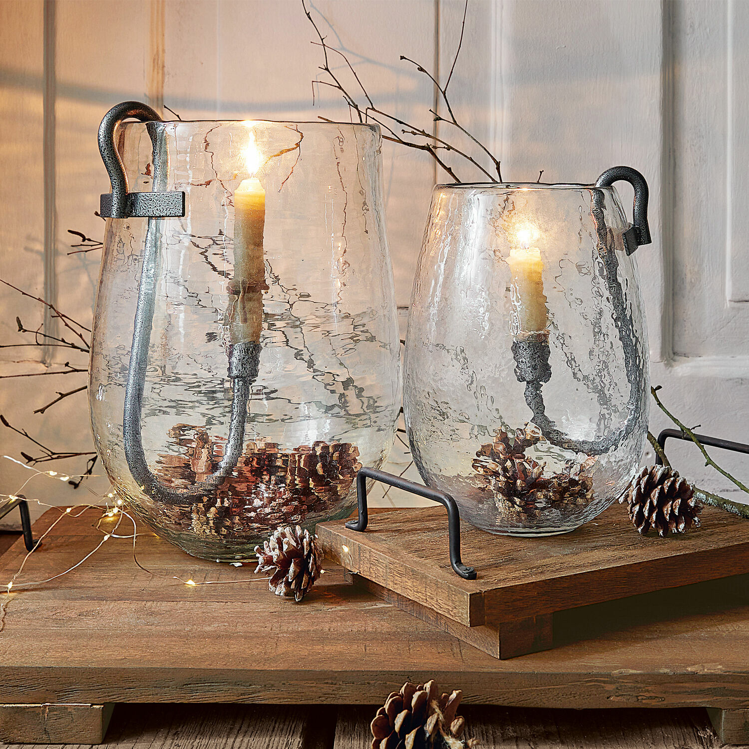 Due lanterne in vetro trasparente con manici in metallo e candele, decorate con pigne