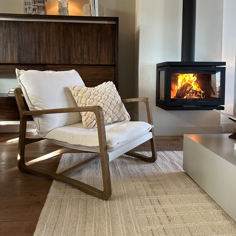 Poltrona in legno con cuscino bianco accanto a camino moderno in soggiorno accogliente