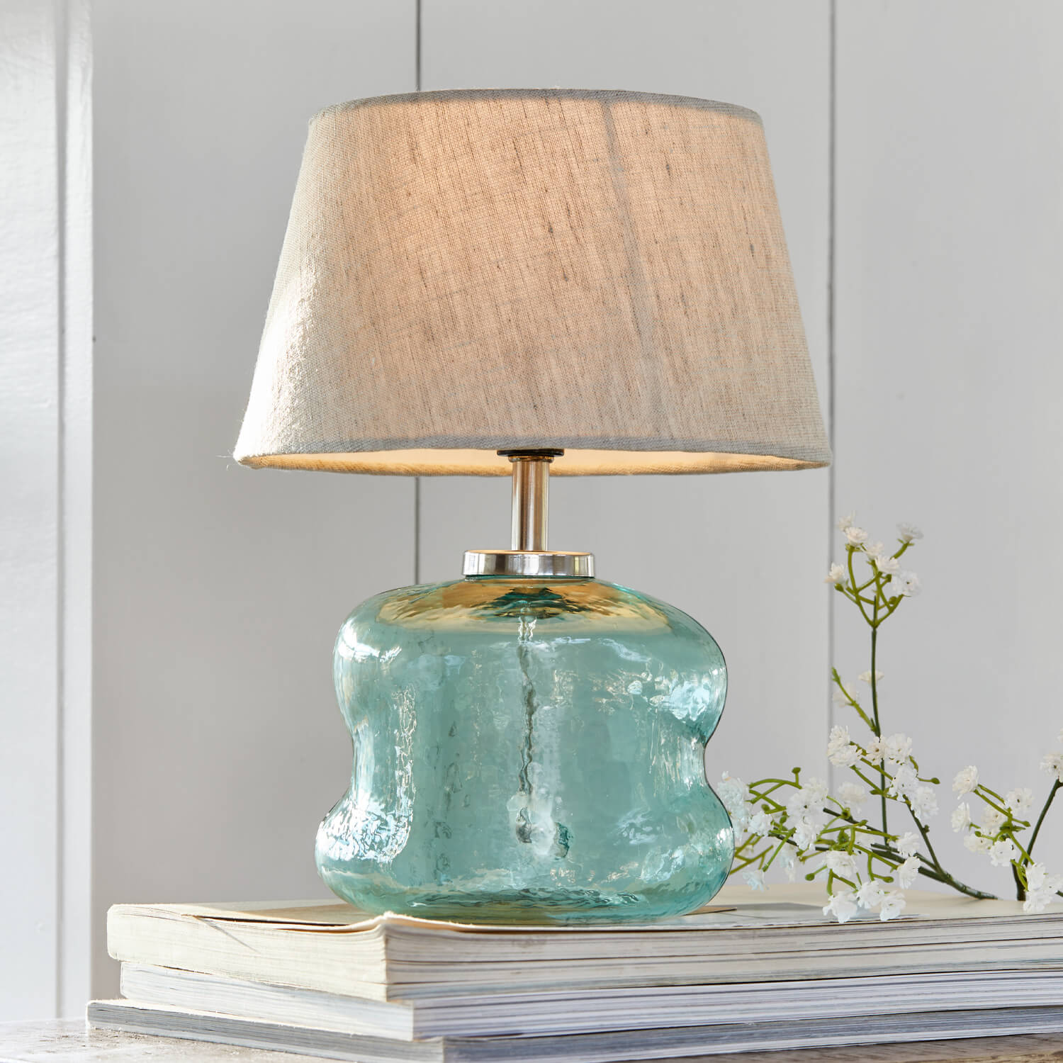 Lampada da tavolo in vetro azzurro con paralume beige su libri, decorazione per interni