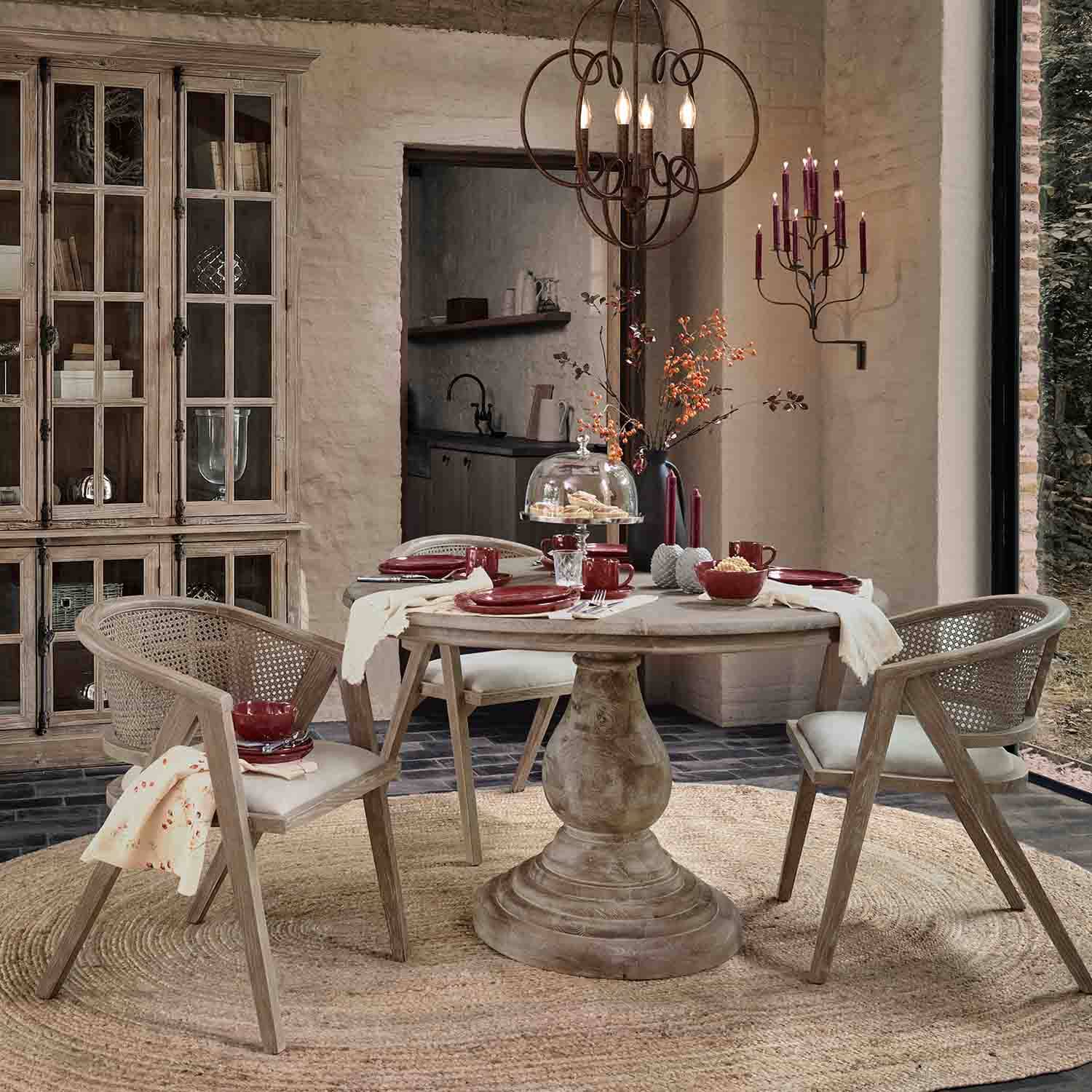 Sala da pranzo con tavolo rotondo in legno e sedie in rattan in tonalità naturali, decorazioni bordeaux