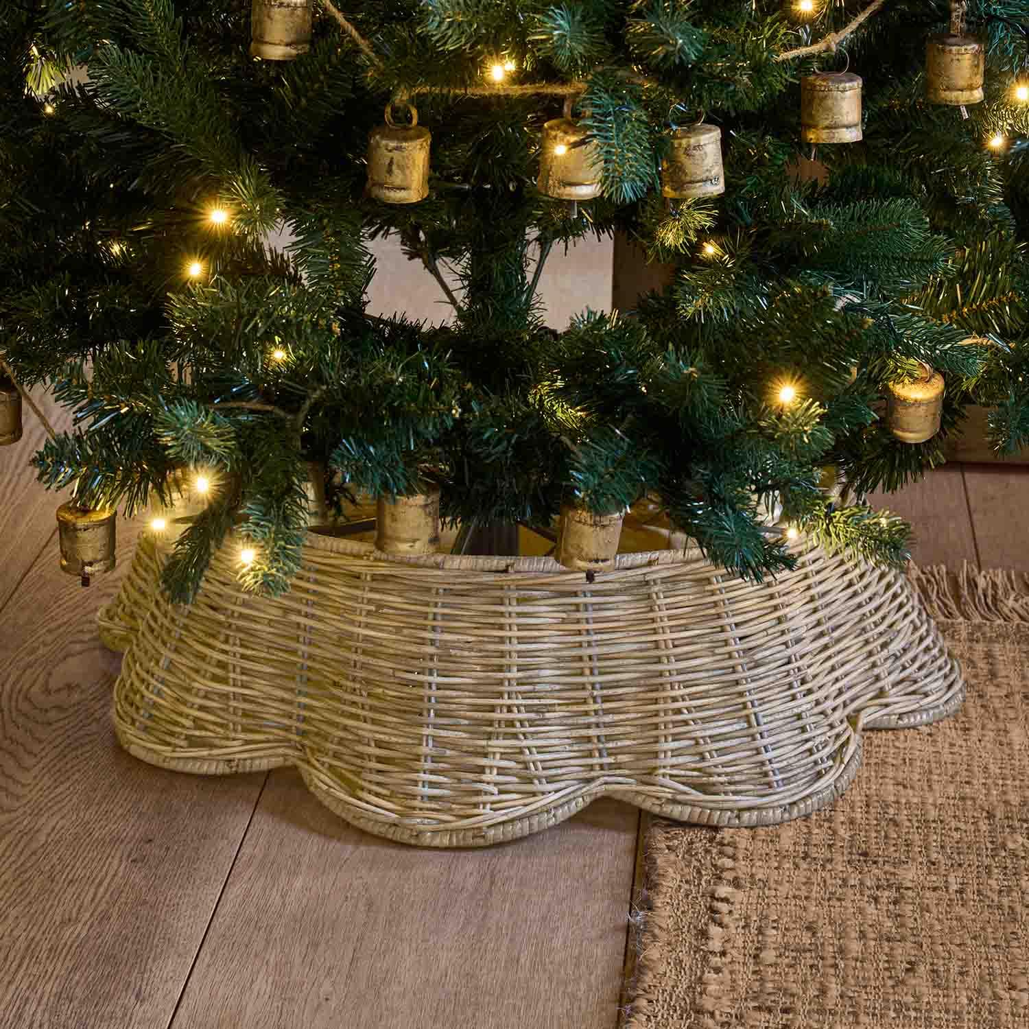 Base per albero di Natale in vimini naturale beige chiaro sotto un albero verde con luci calde