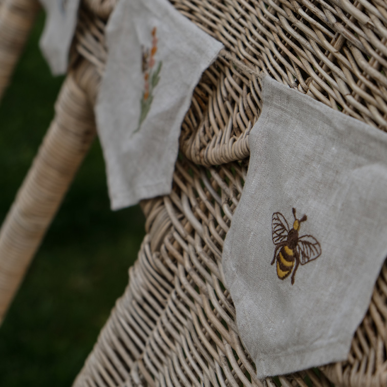 Sacchetti decorativi in lino con ricamo ape e fiori su sedia in vimini beige