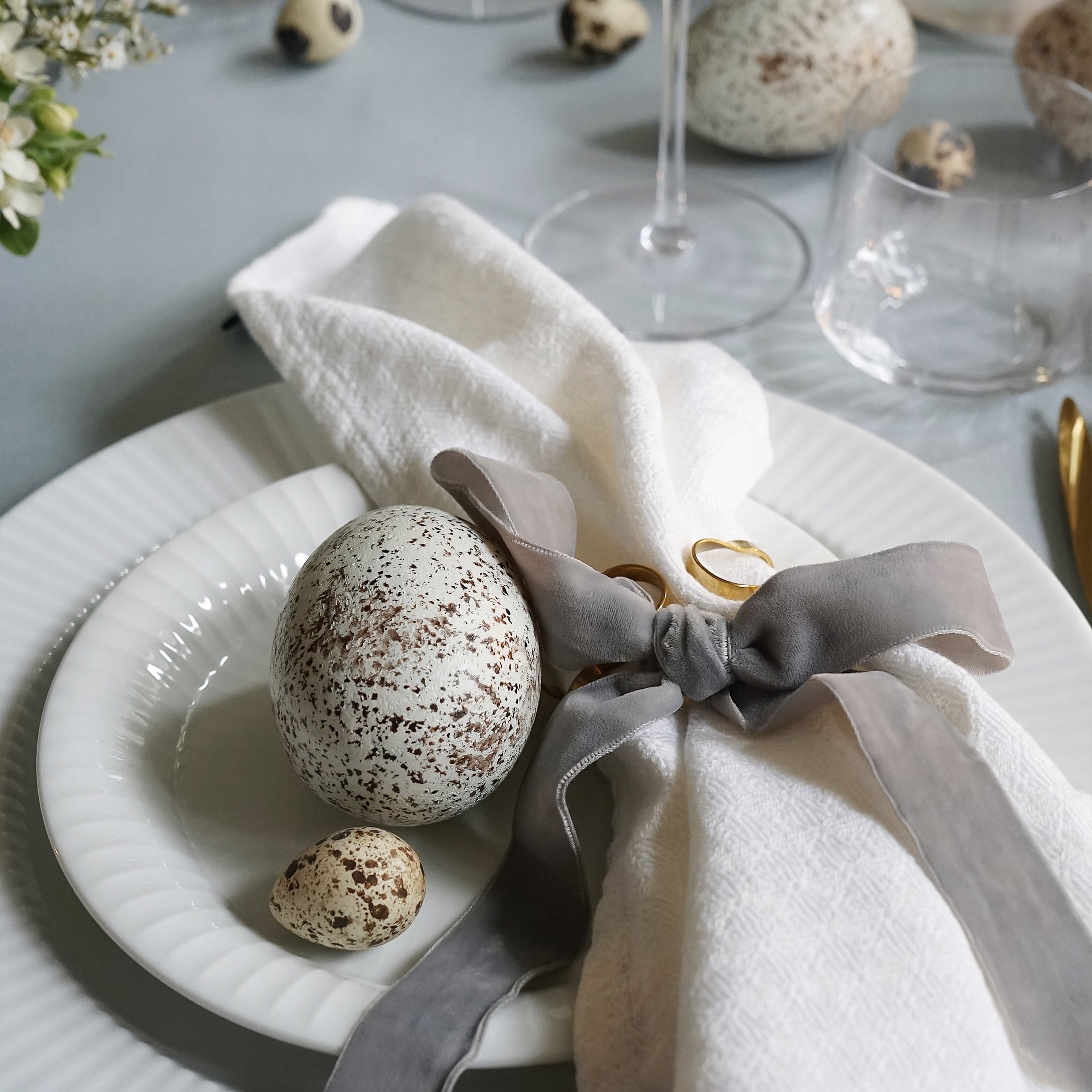 Piatti bianchi con uova macchiate decorative e tovagliolo di lino con fiocco grigio sul tavolo