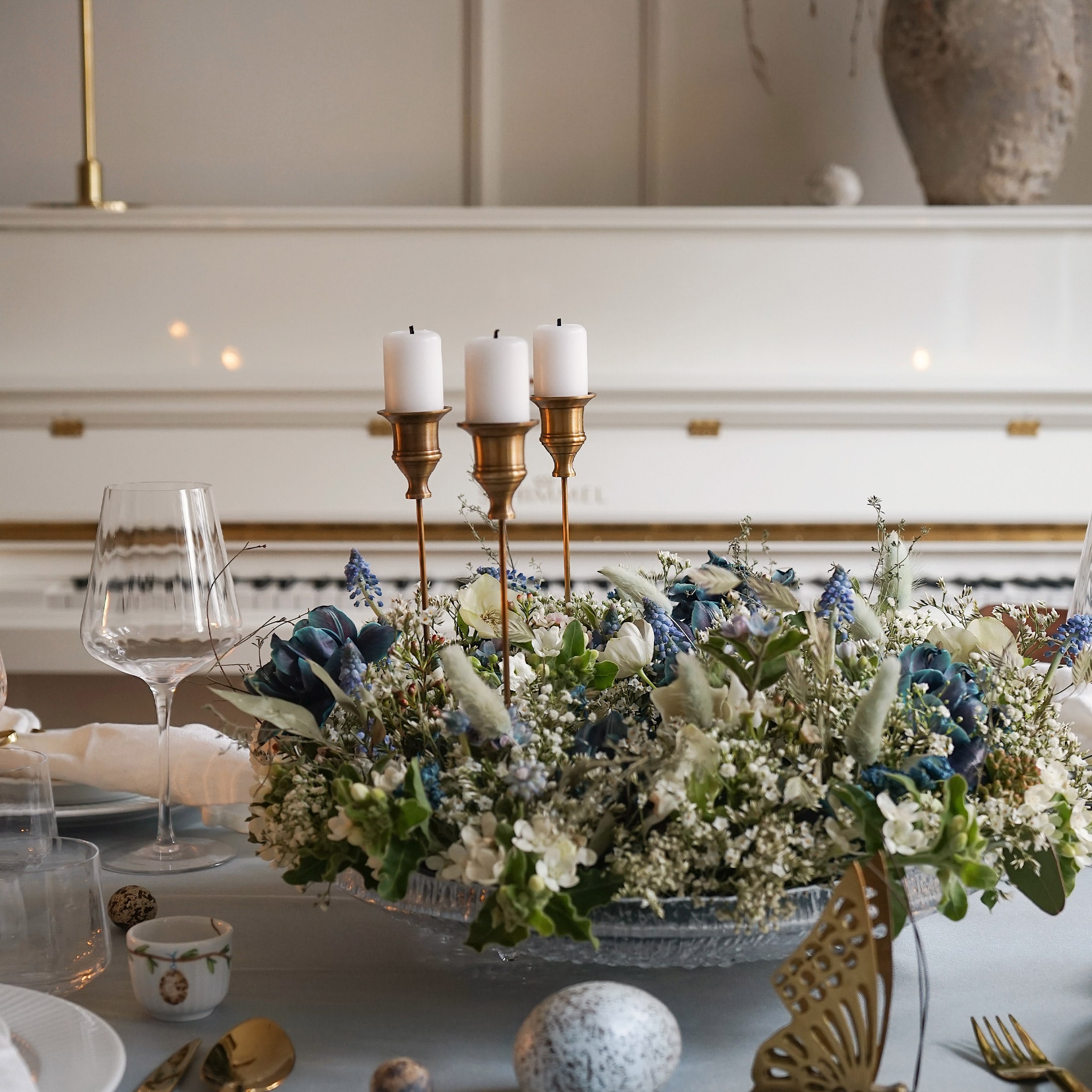 Portacandele decorativo con tre candele bianche e composizione floreale su base di vetro
