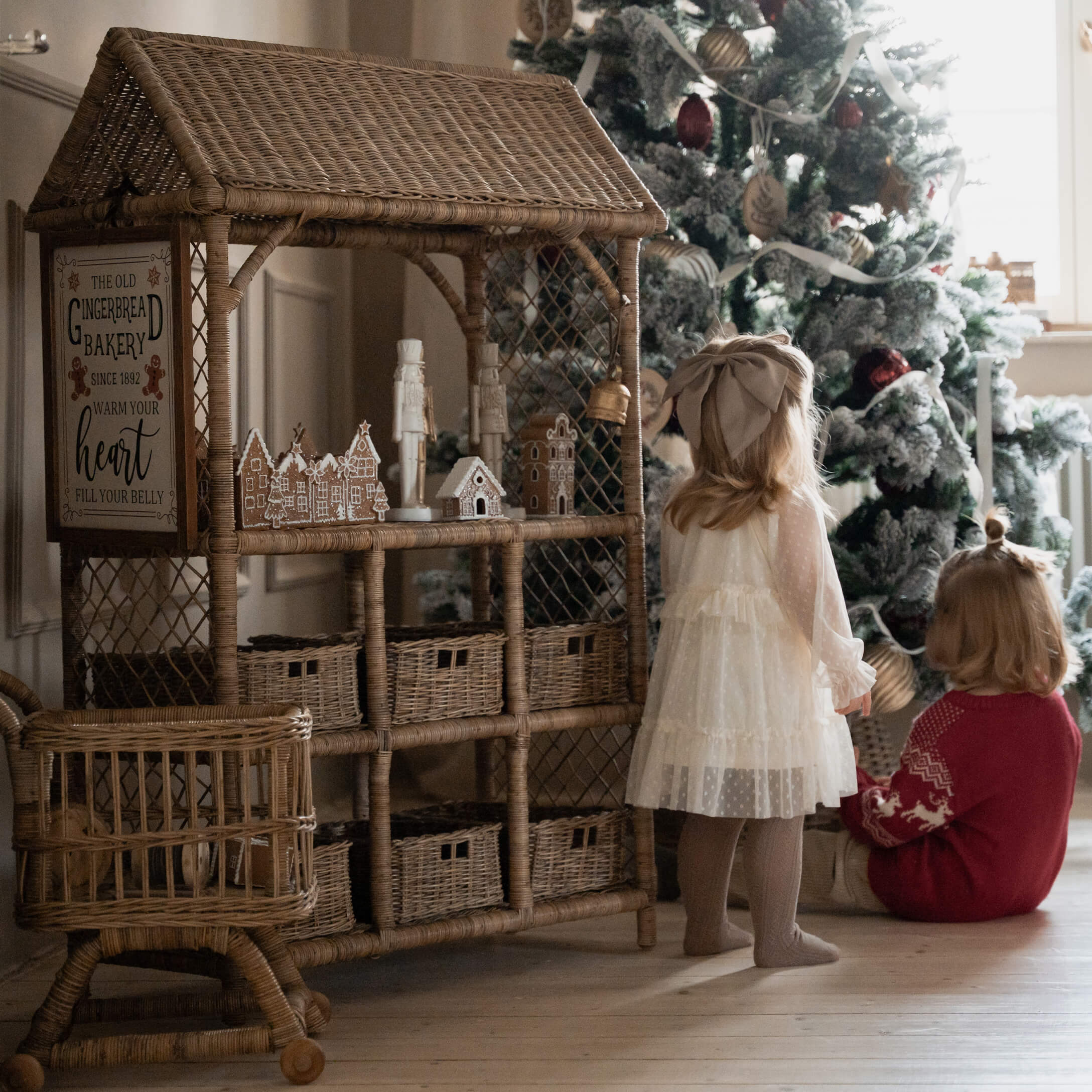 Casetta in vimini con decorazioni di pan di zenzero accanto a bambini davanti all'albero di Natale
