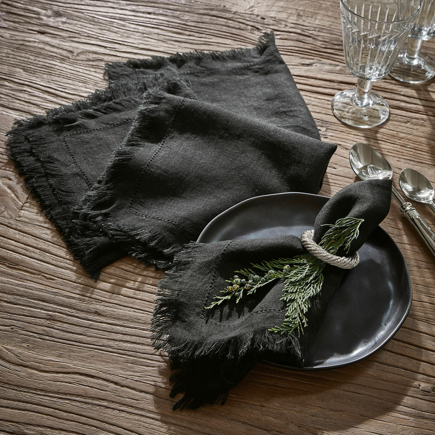 Set di 4 tovaglioli Pibrac Tovaglioli neri in lino con frange su tavolo in legno con decorazione di rami verdi
