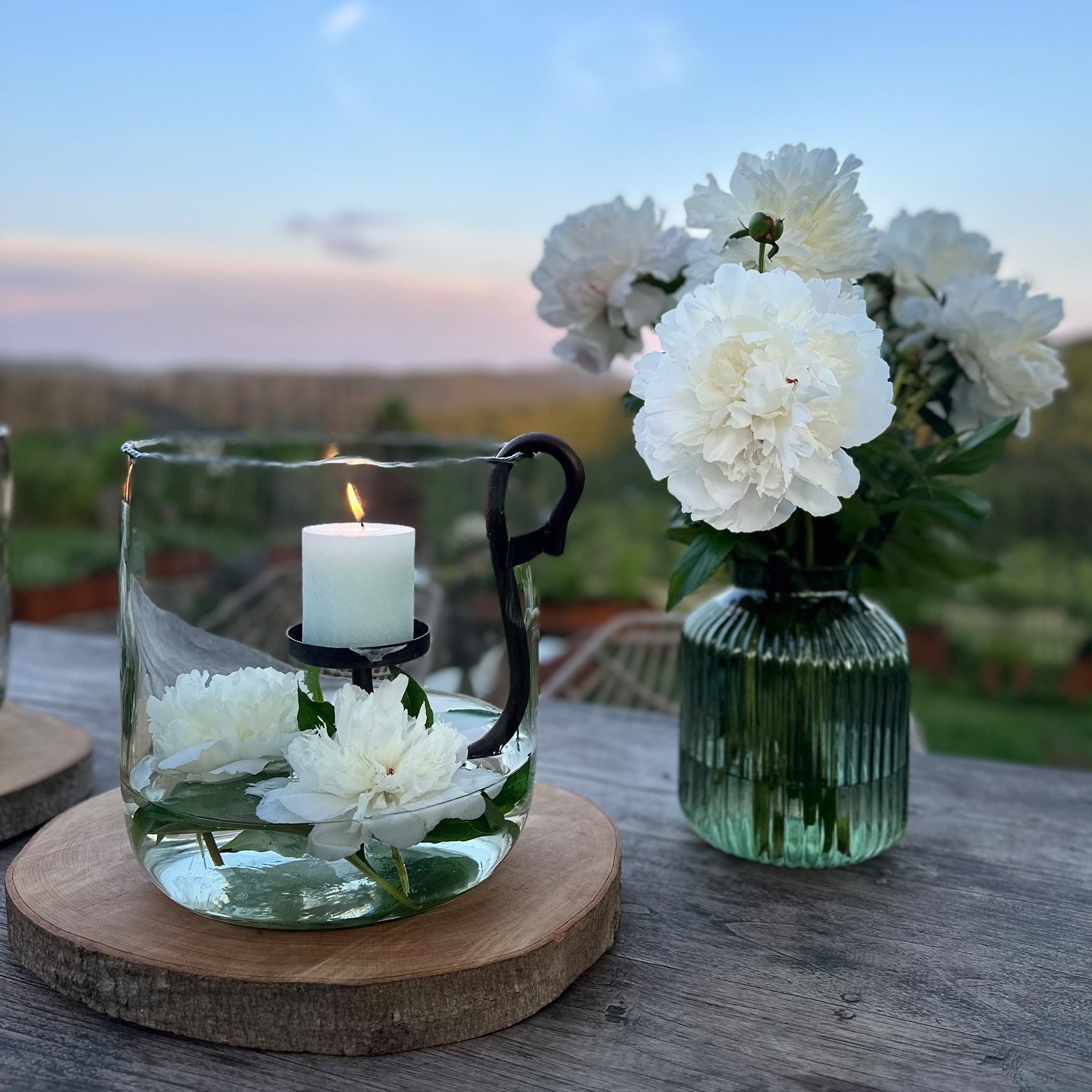 Portacandele in vetro con candela bianca e fiori bianchi su base in legno all'aperto
