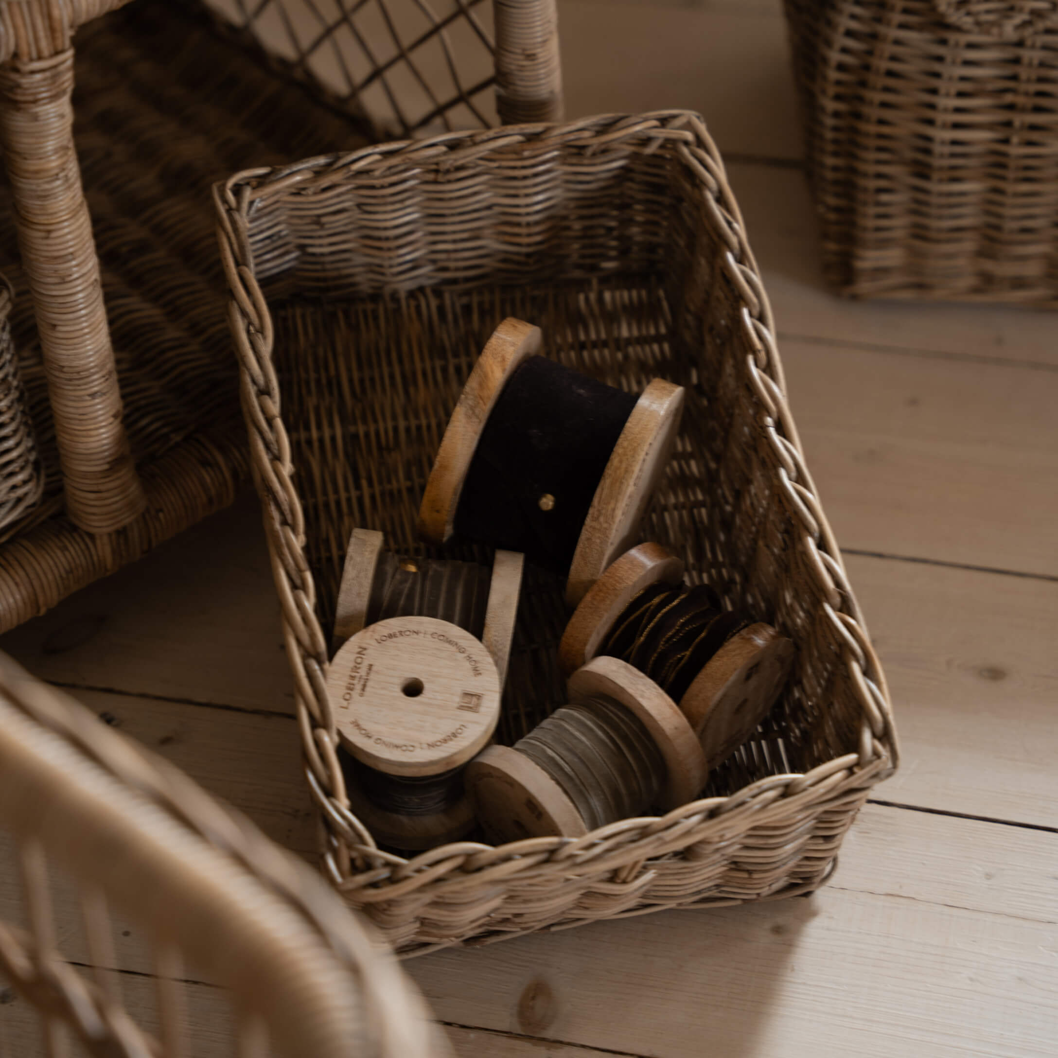 Cesto in vimini con rocchetti di legno con filo nero e grigio su pavimento in legno chiaro
