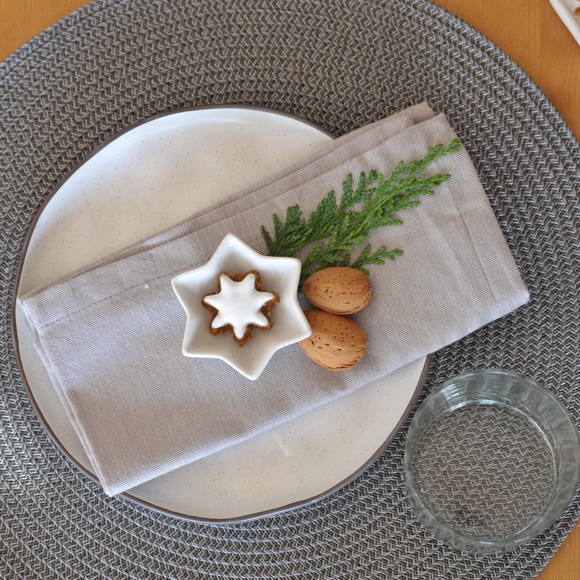 Tovaglietta grigia intrecciata con piatto bianco, tovagliolo di lino e decorazione natalizia