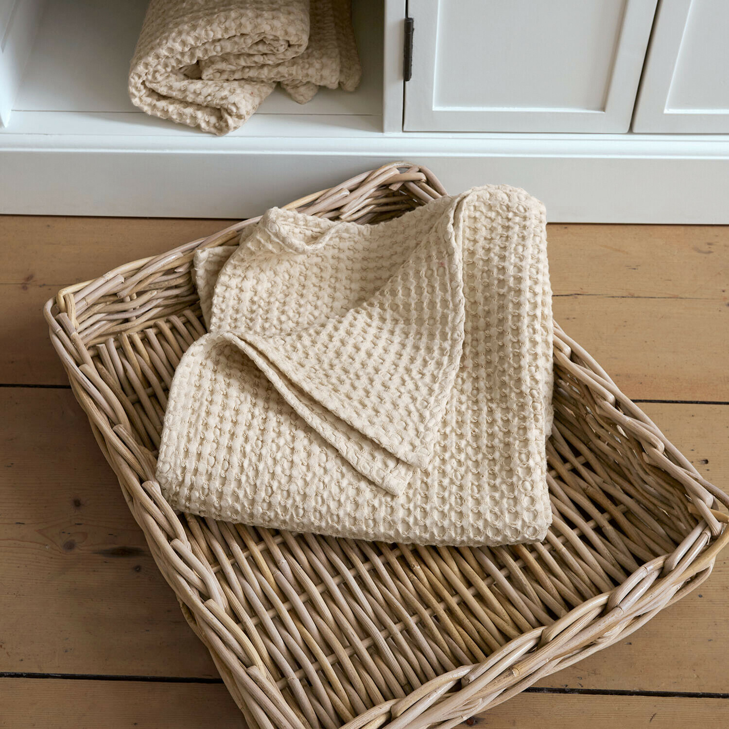 Asciugamano Maralei Coperta beige in cotone a nido d'ape in cesto di vimini su pavimento in legno chiaro