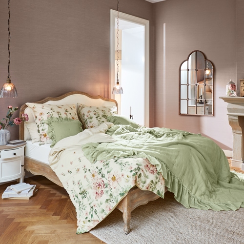 Camera da letto con letto in legno, biancheria da letto verde e floreale, lampada sospesa e specchio decorativo a parete
