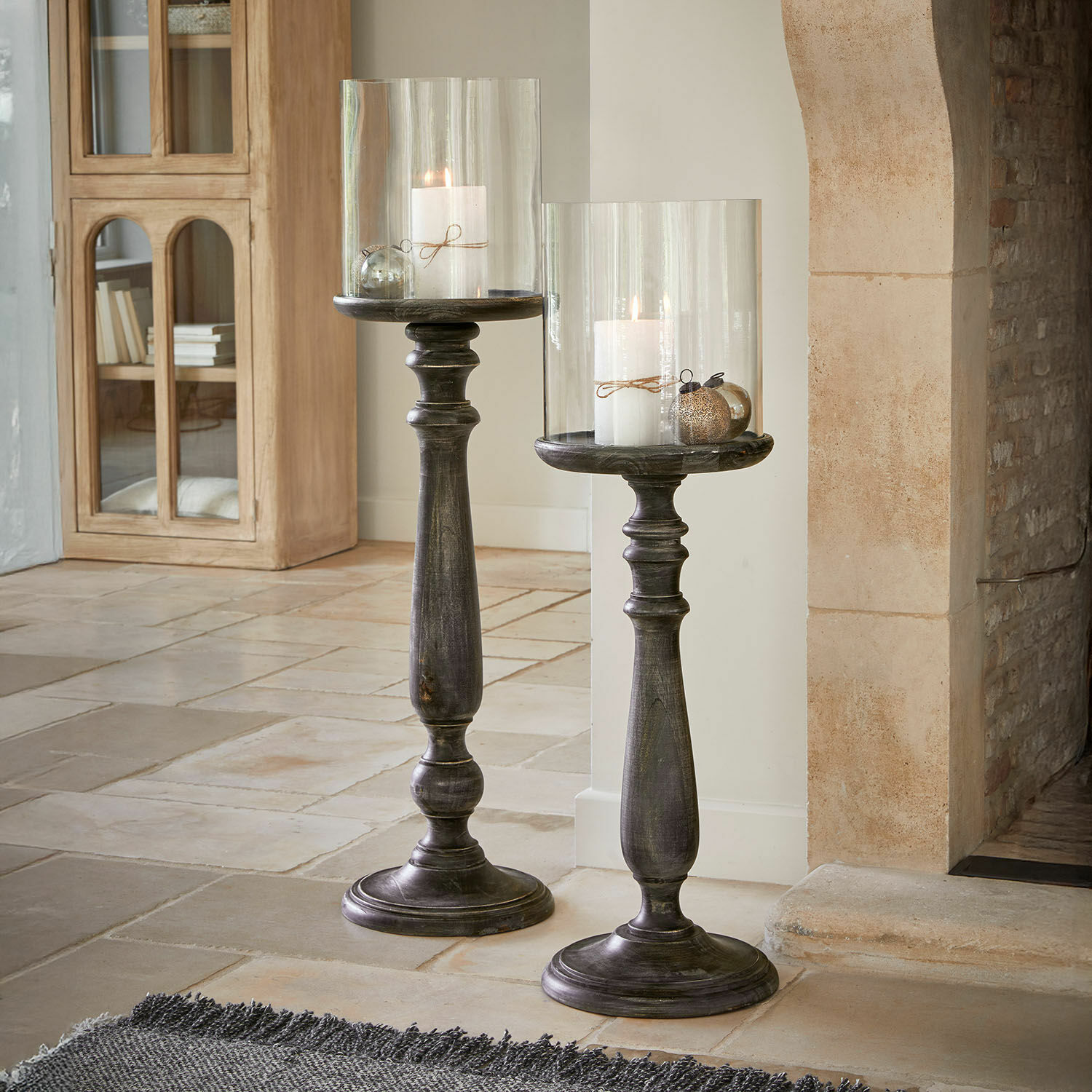 Coppia di candelieri Reville Due alti portacandele in legno scuro con coperture in vetro trasparente e candele bianche in soggiorno