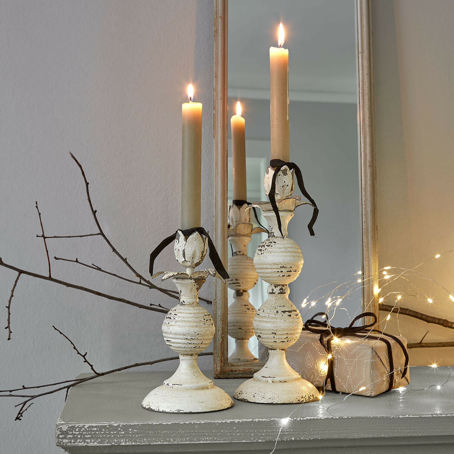 Coppia di portacandele Soliras Due candelabri in metallo crema con candele beige e nastro nero su mensola grigia con luci decorative
