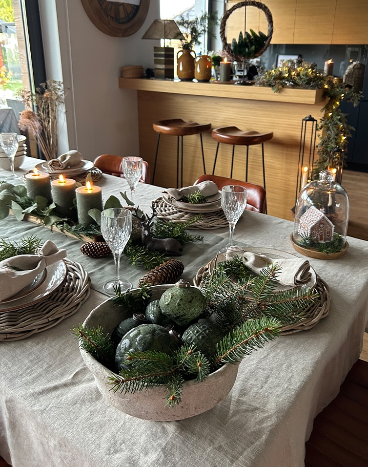 Tavola decorata per Natale con rami verdi naturali e candele in un ambiente accogliente