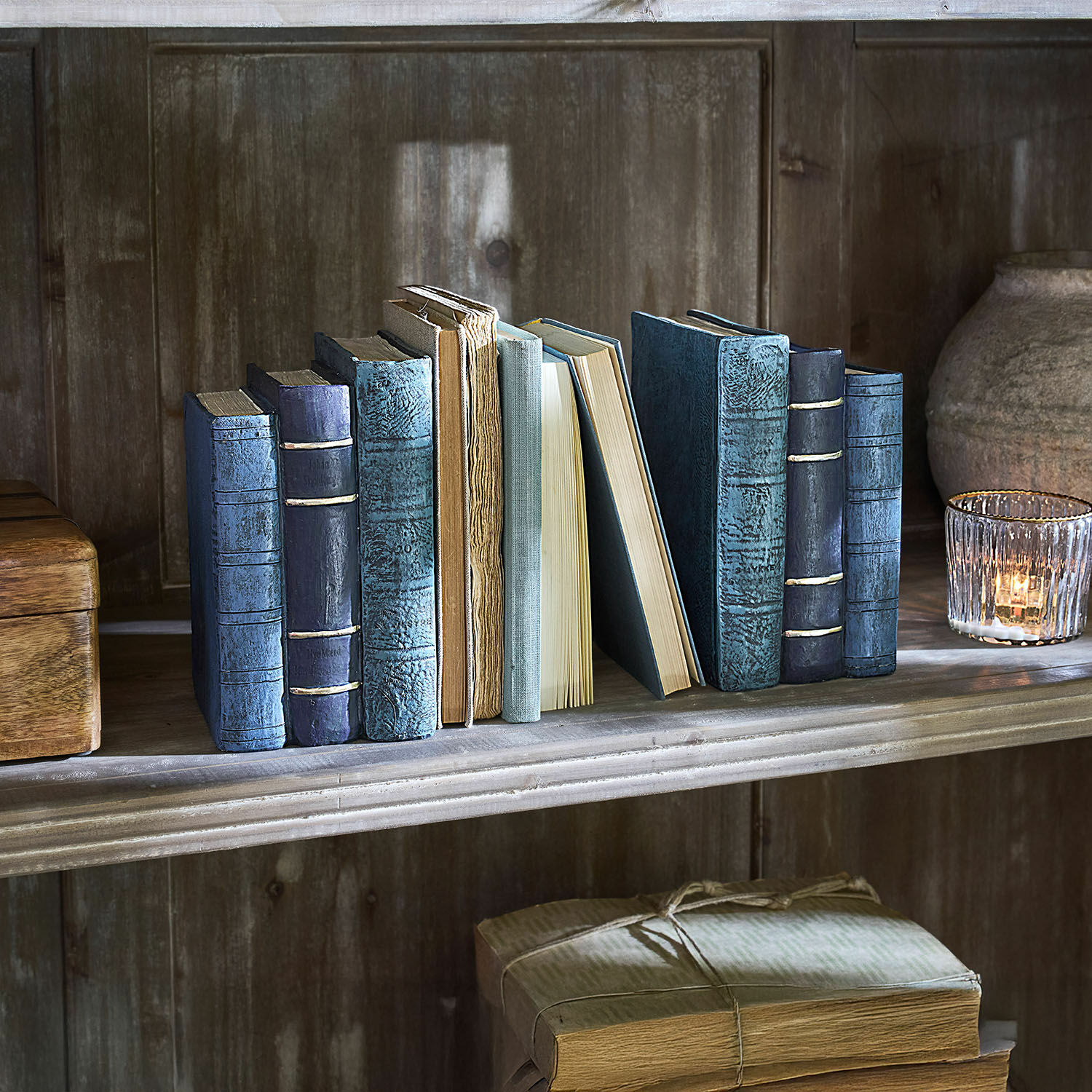 Coppia di fermalibri Morvini Collezione di vecchi libri con copertine blu e beige su una mensola di legno con un portacandela