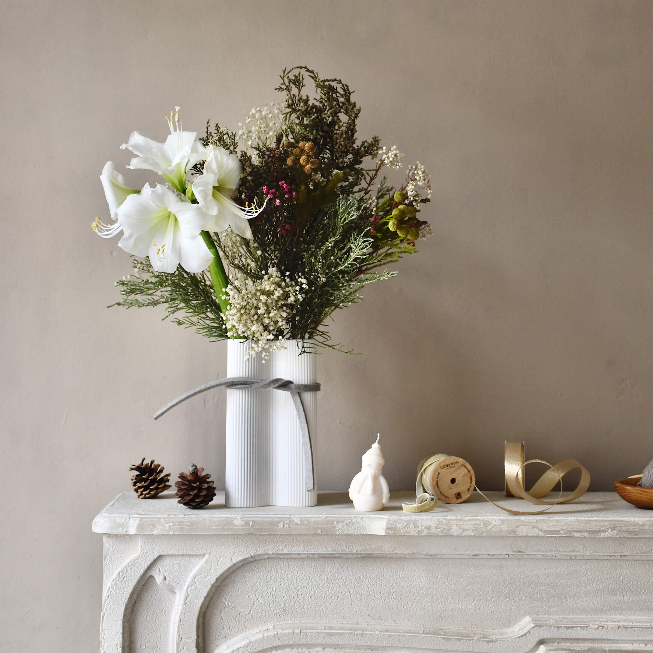 Vaso in ceramica bianca con fiori bianchi e rami verdi su un camino bianco decorativo