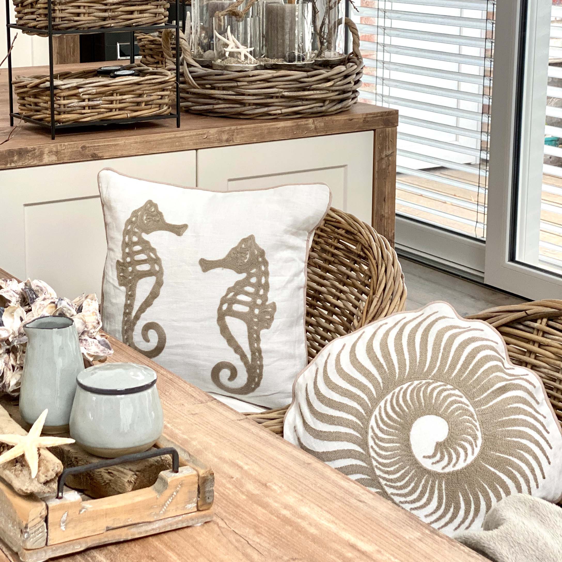 Cuscini decorativi con motivi di cavallucci marini e conchiglie su sedia in vimini in ambiente luminoso