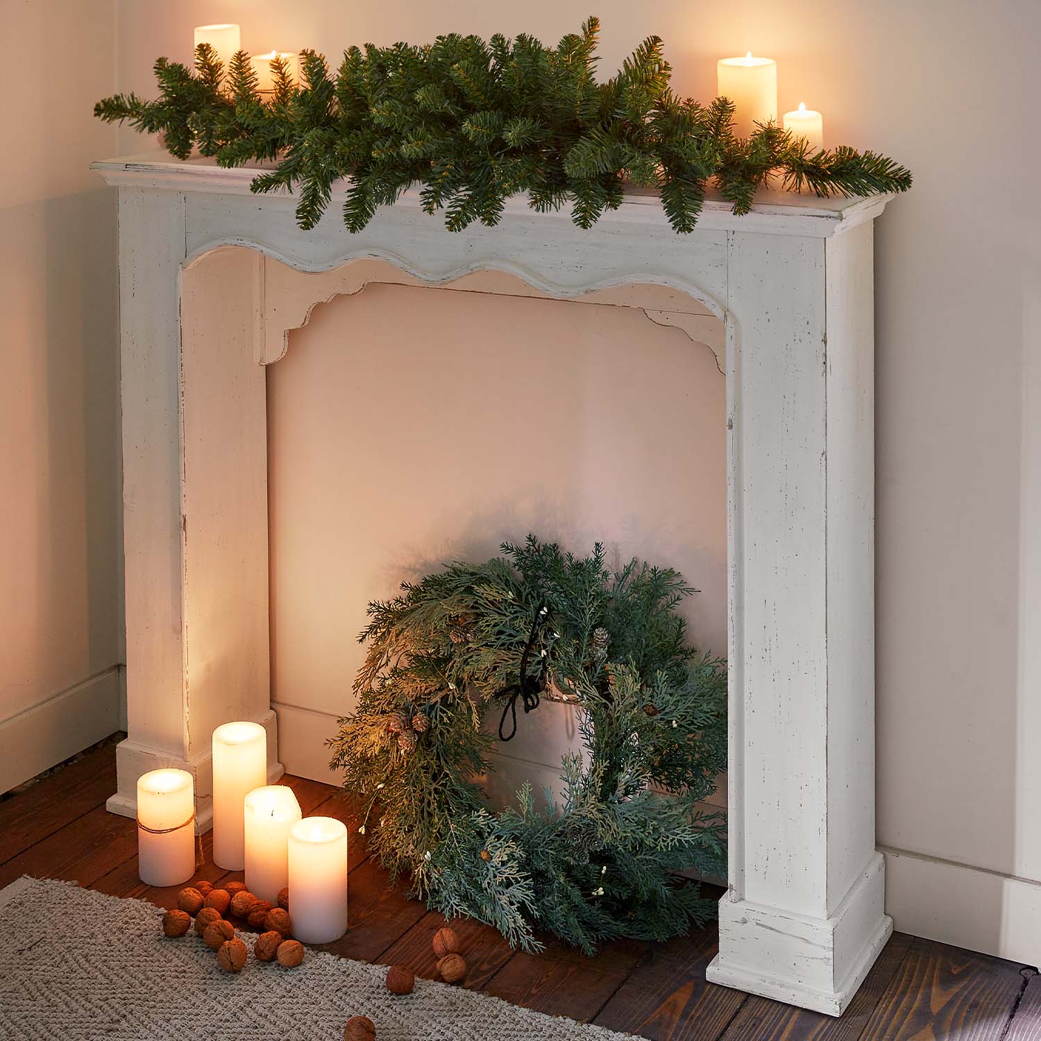 Cornice camino in legno bianco con corona verde e candele accese su pavimento in legno, decorazione natalizia