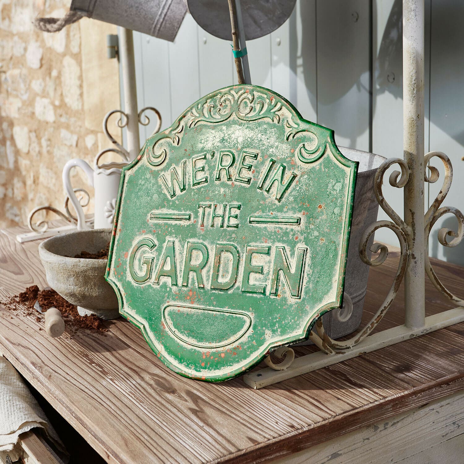 Targa decorativa Merrin Targa decorativa in metallo verde con scritta We're in the Garden su tavolo di legno in giardino