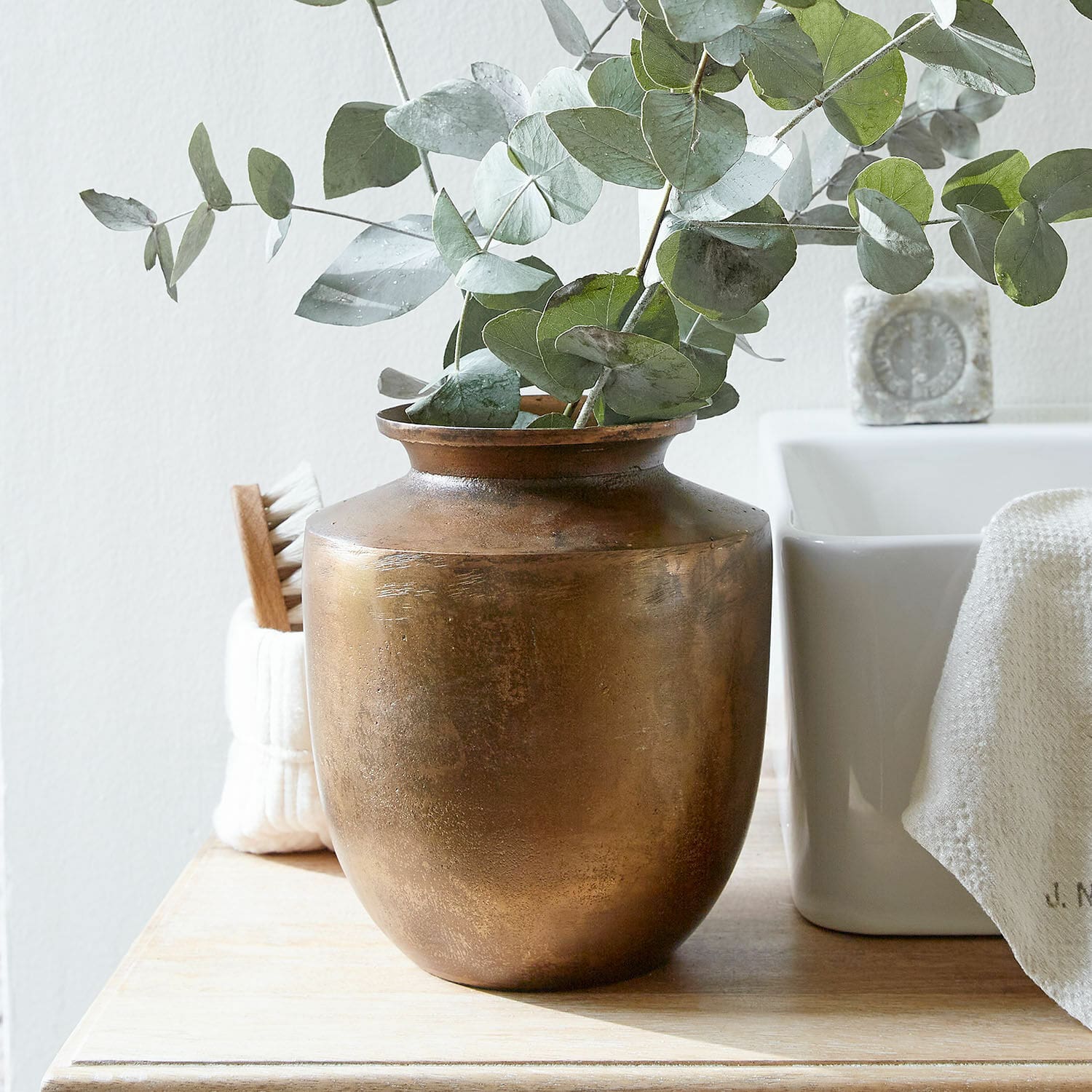 Vaso Toulane Vaso in ottone con foglie verdi di eucalipto su tavolo in legno in ambiente luminoso