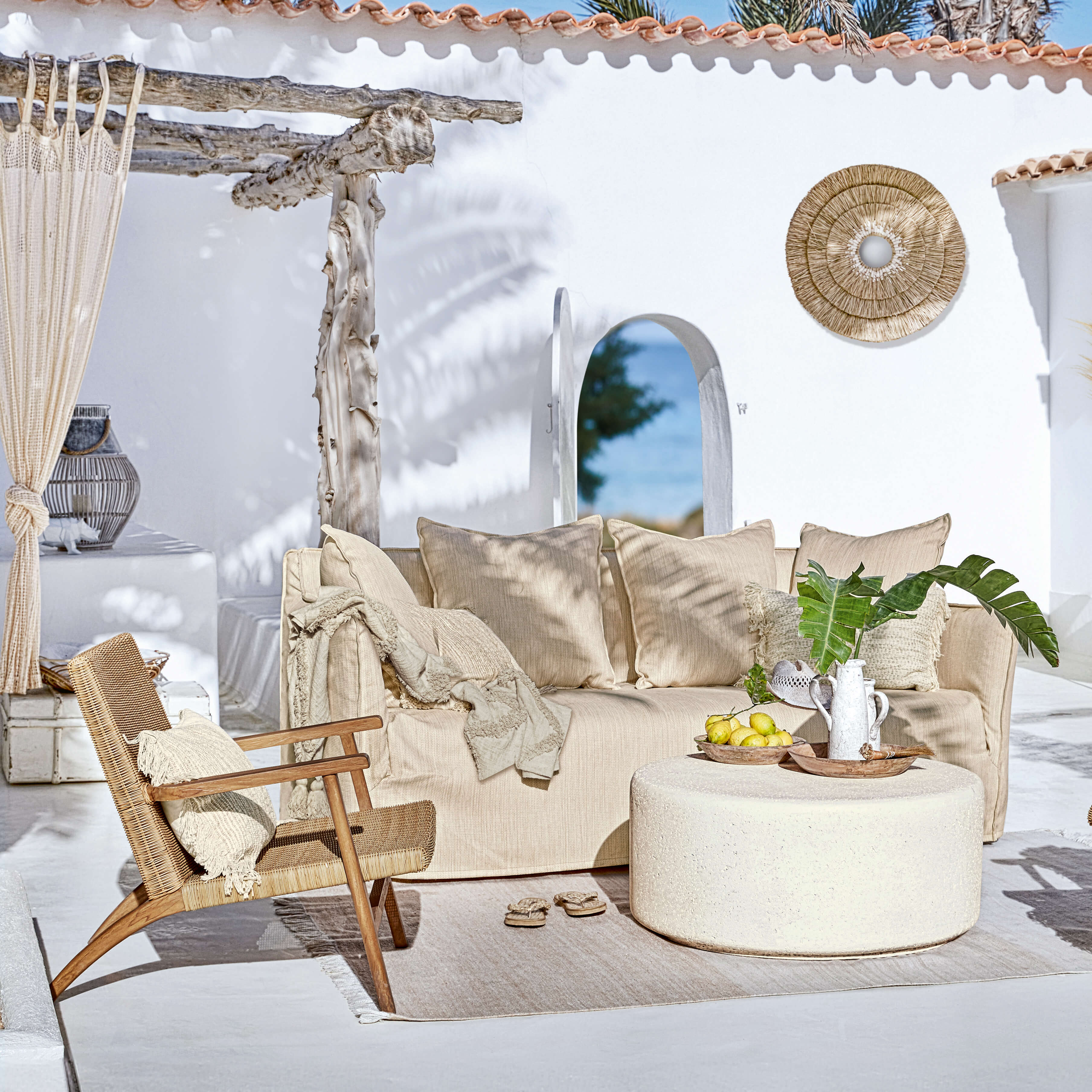 Divano beige e poltrona in rattan su terrazza con decorazioni naturali e tavolino rotondo