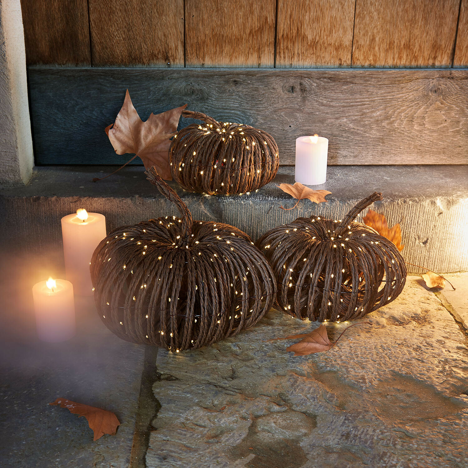 Set di 3 zucche a LED Ysolann Zucca decorativa in corda scura con luci LED soffuse e candele su pavimento in pietra rustica