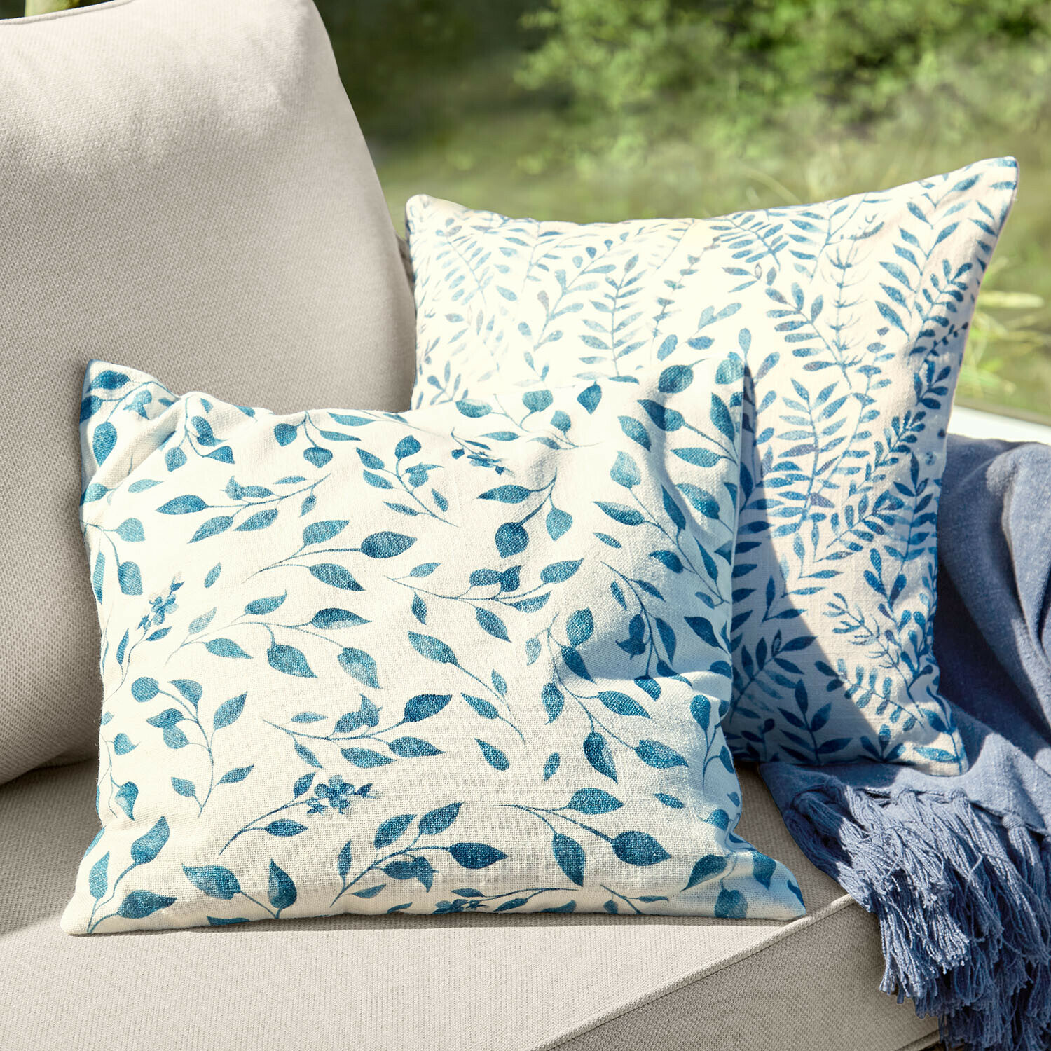 Coppia di copricuscini Ocevara Due cuscini decorativi in cotone crema con motivo foglie blu su divano beige