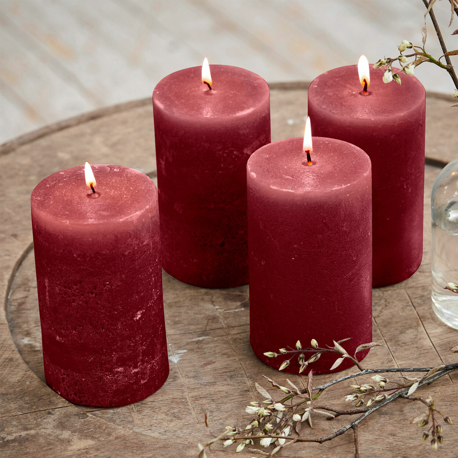 Set di 4 candele Braga Quattro candele rosse in cera su tavolo di legno con decorazione floreale, atmosfera accogliente