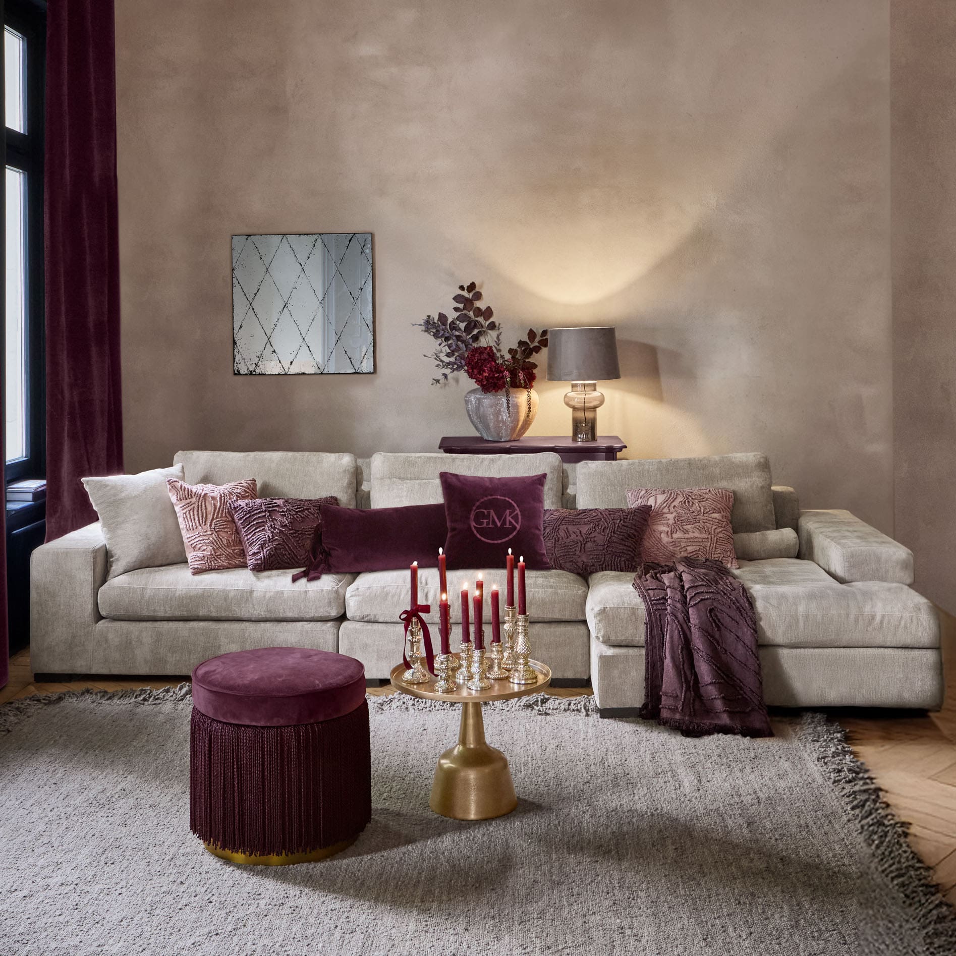 Soggiorno accogliente con divano beige, cuscini bordeaux e tavolino dorato con candele rosse