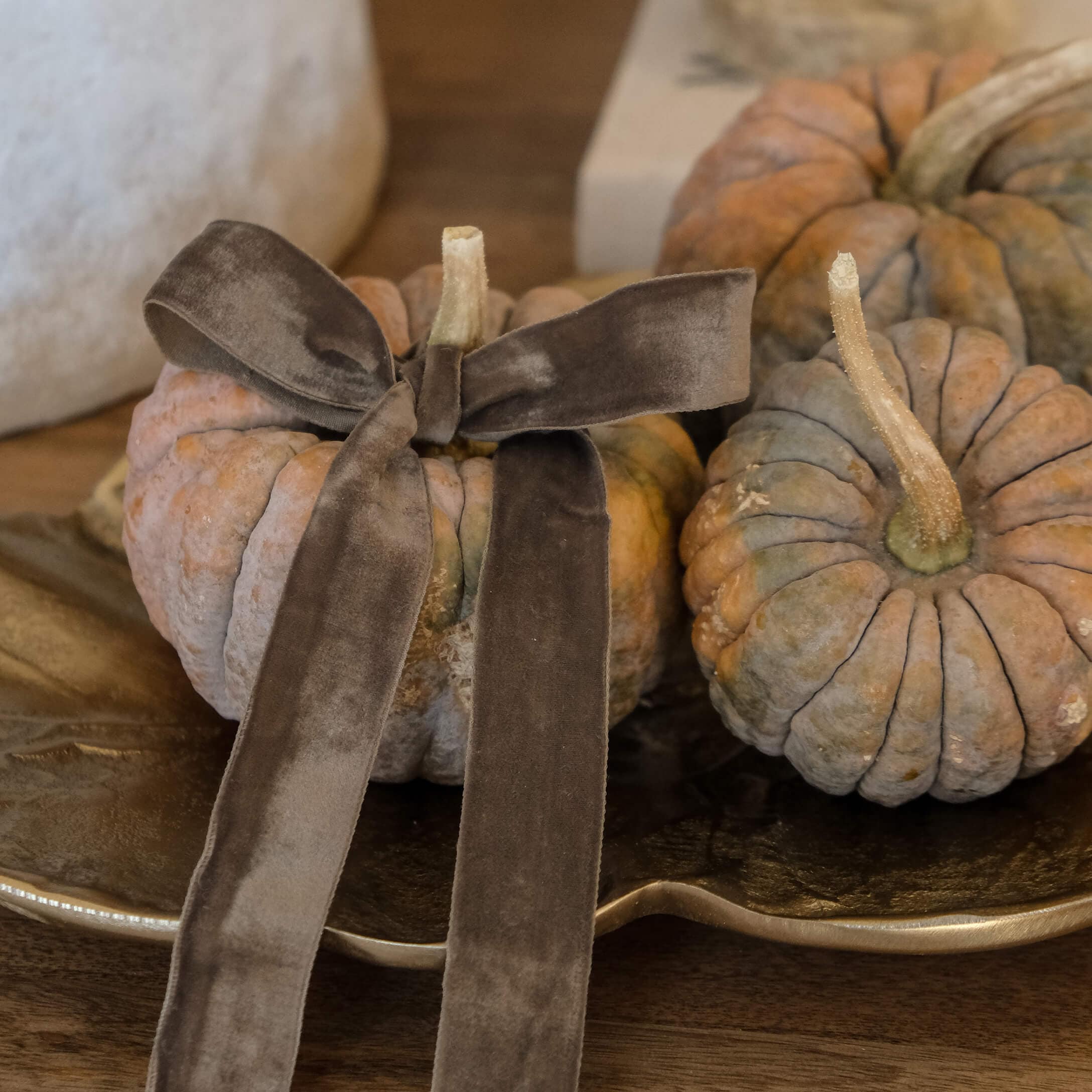 Zucca decorativa arancione-grigia con fiocco di velluto marrone su vassoio dorato su tavolo in legno