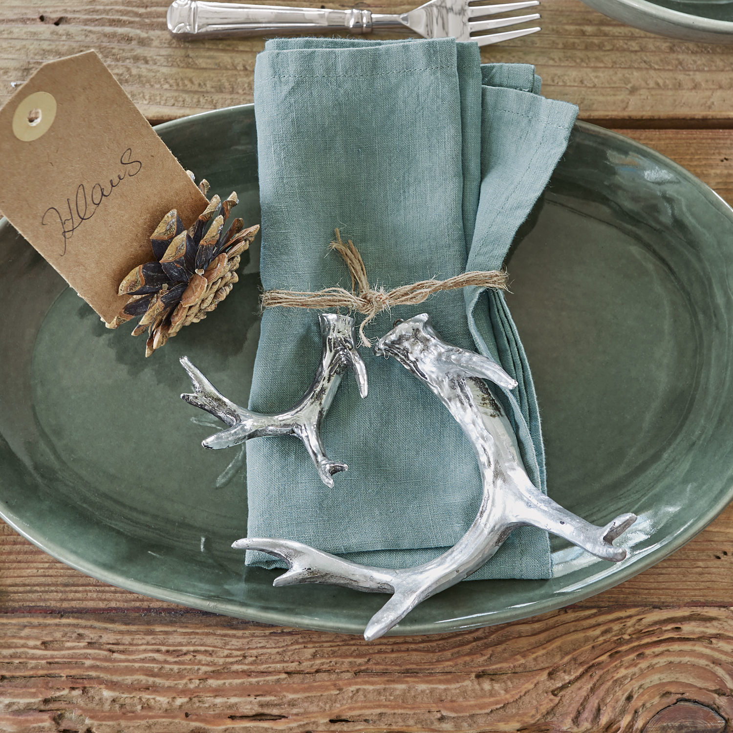 Coppia di corna di cervo decorative Tiana Ciotola in ceramica verde con tovagliolo di lino e decorazioni argentate a forma di corna su tavolo di legno