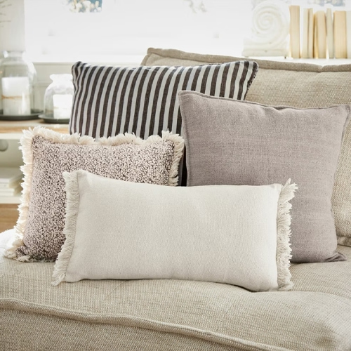 Set di quattro cuscini decorativi in tonalità neutre su divano beige, tessuti per il soggiorno