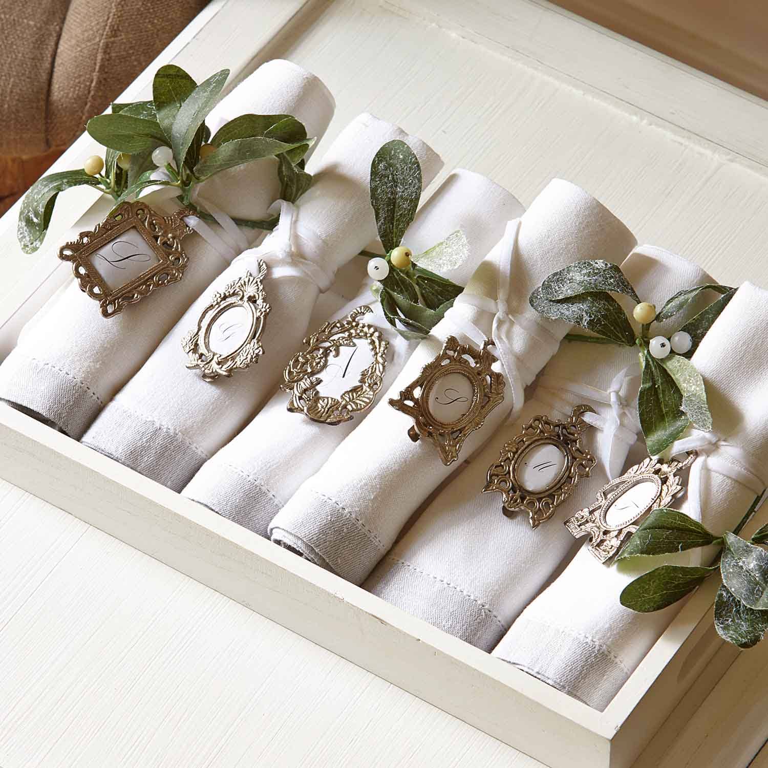 Tovaglioli di lino bianchi con anelli decorativi in metallo e foglie verdi per tavola elegante.