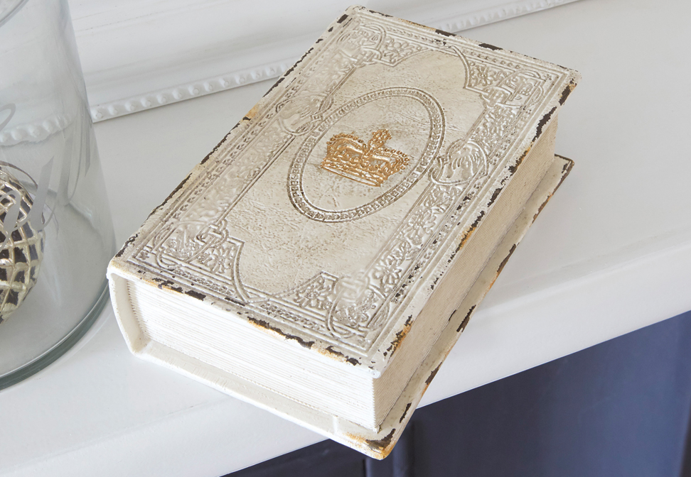 Libro decorativo shabby chic con copertina bianca invecchiata e corona dorata su mensola
