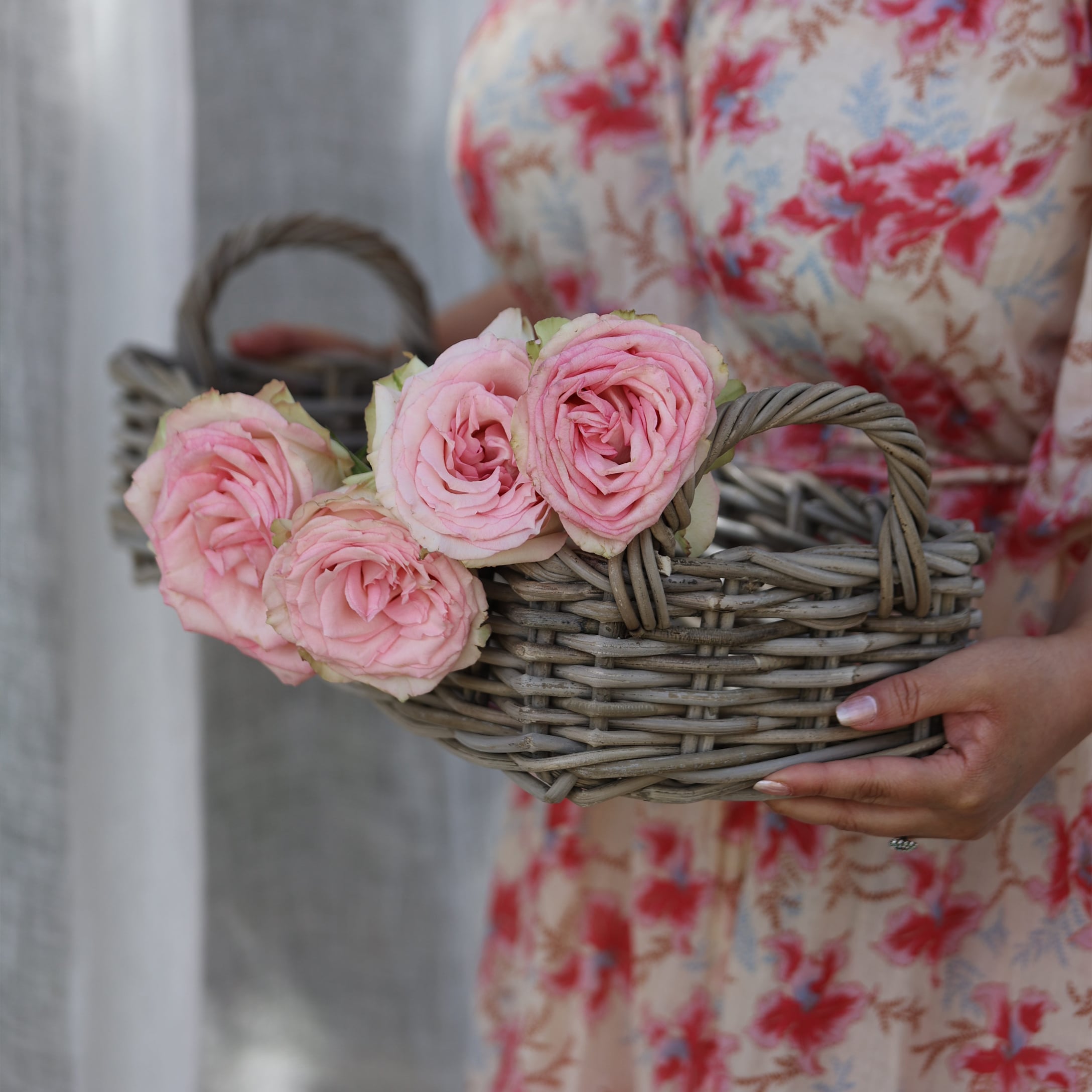 Piccolo cesto in vimini grigio con rose rosa tenuto da persona con vestito floreale