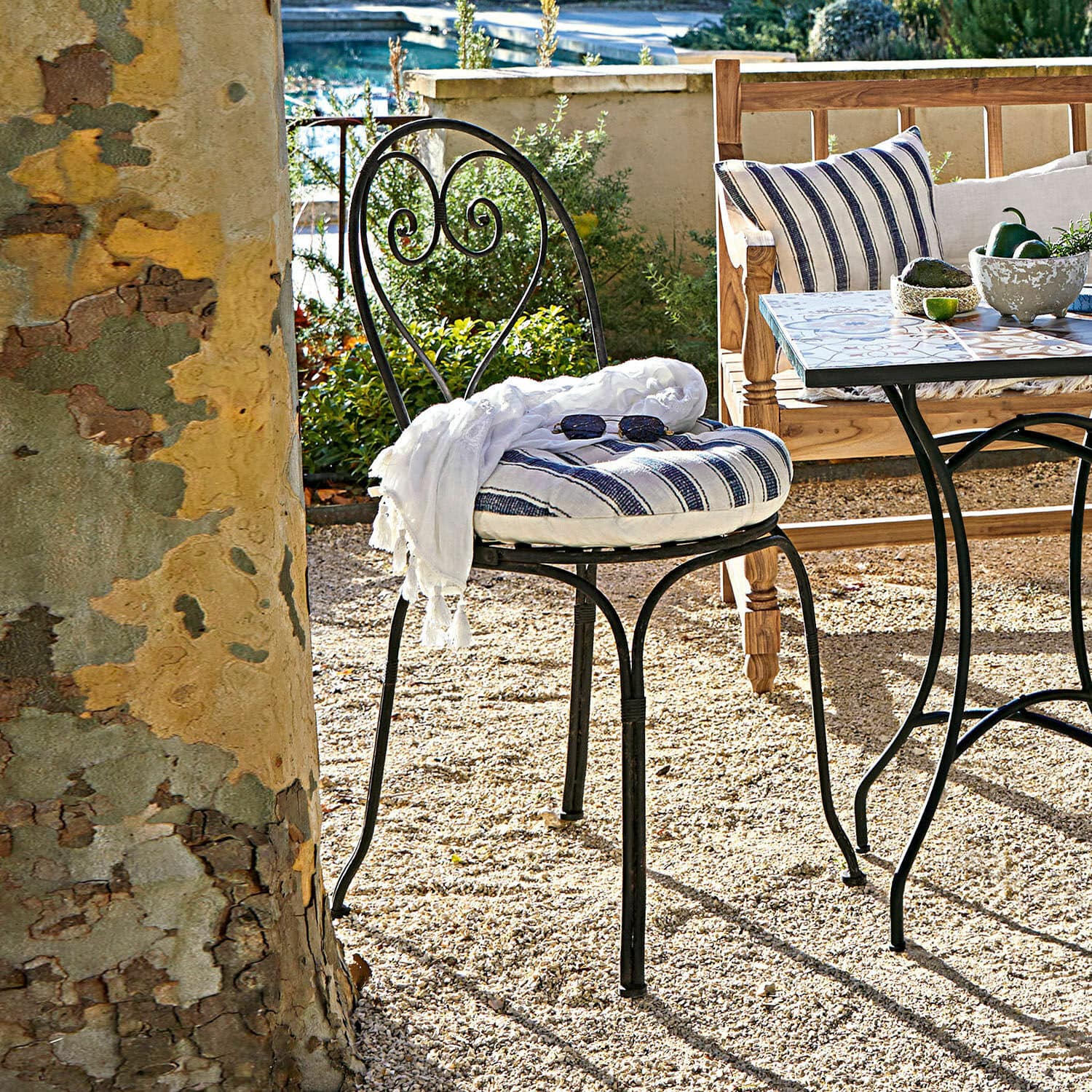 Sedia Aube Sedia da giardino in metallo nero con cuscino a righe e sciarpa bianca su patio ghiaioso