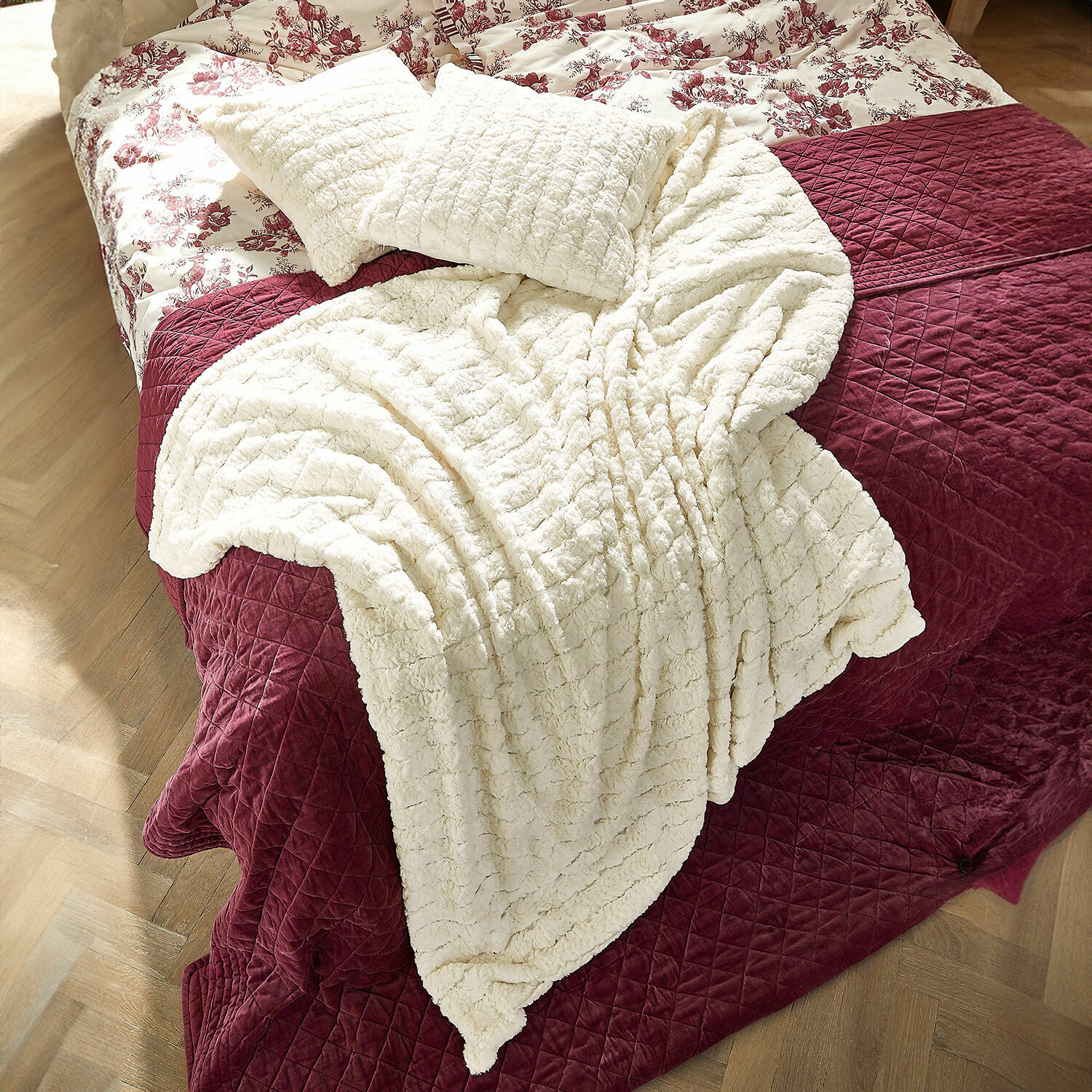 Plaid Dorelice Coperta e cuscini in peluche crema su copriletto trapuntato bordeaux sul letto
