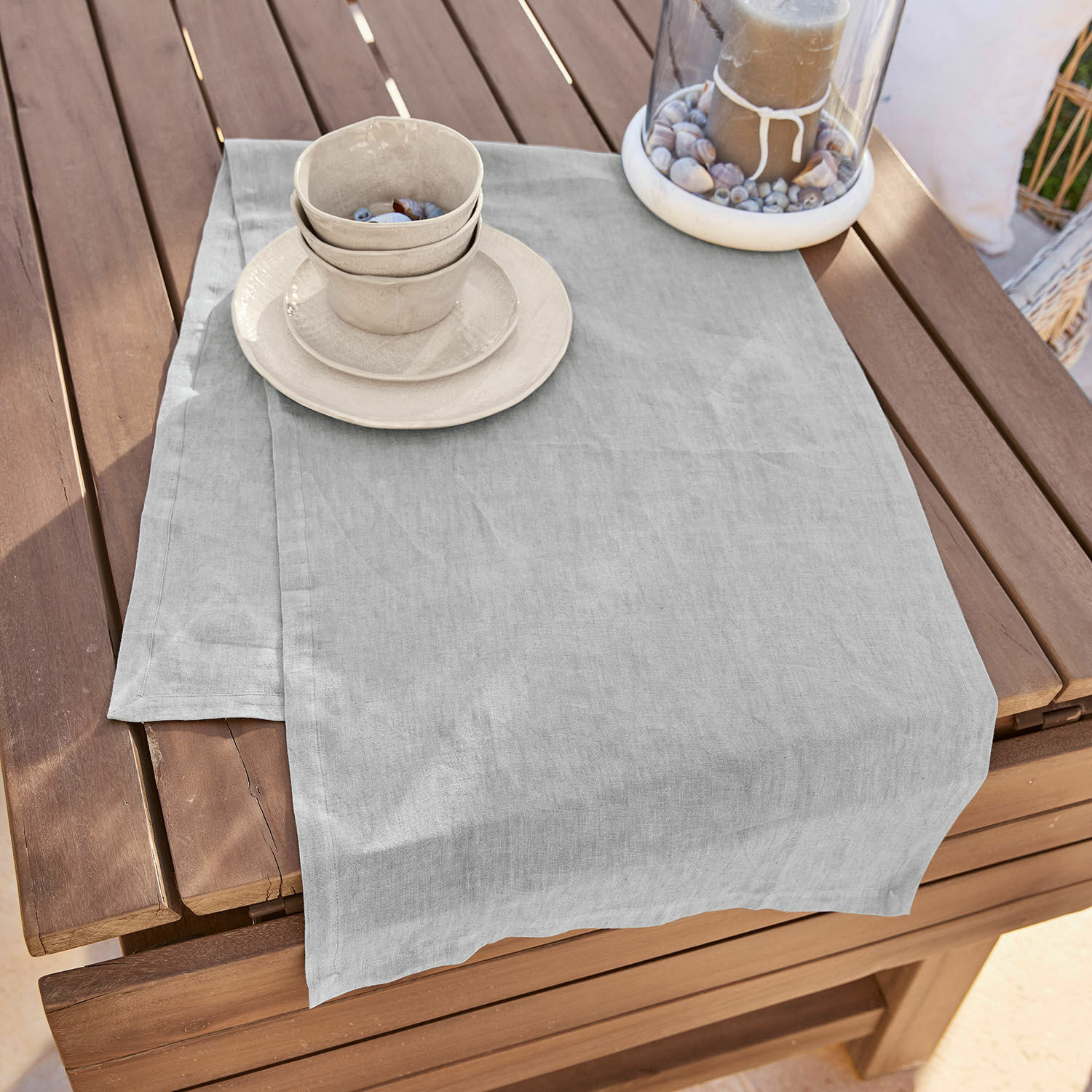 Runner Bursinel Tovaglia in lino grigio chiaro su tavolo in legno con stoviglie in ceramica e candela decorativa