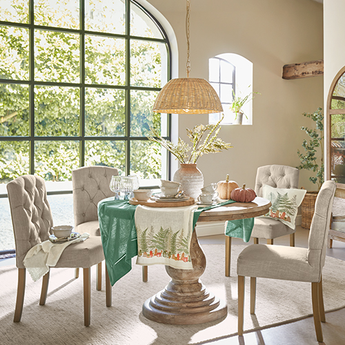 Sala da pranzo con tavolo rotondo in legno e sedie imbottite beige, decorazioni naturali e luce naturale