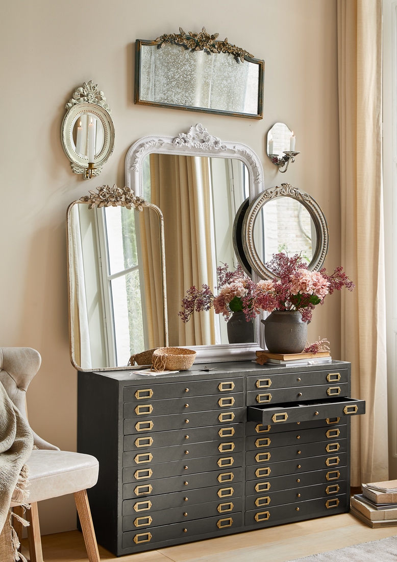 Cassettiera nera in metallo con molti cassetti e specchi decorativi vintage appesi al muro