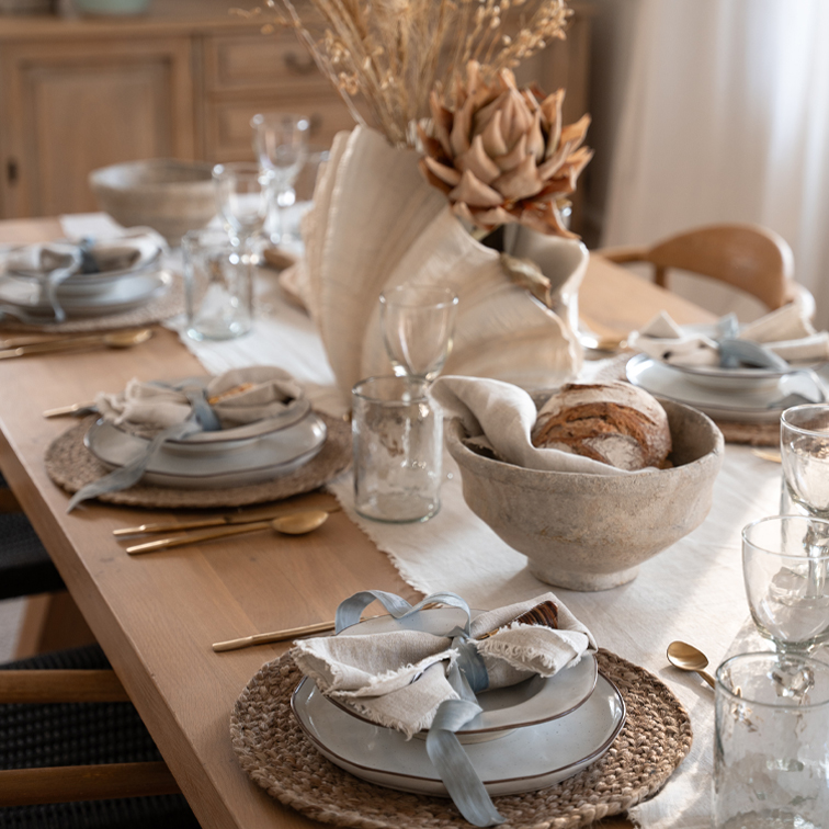 Tavolo rustico in legno con piatti in ceramica, tovaglioli di lino e decorazioni floreali essiccate