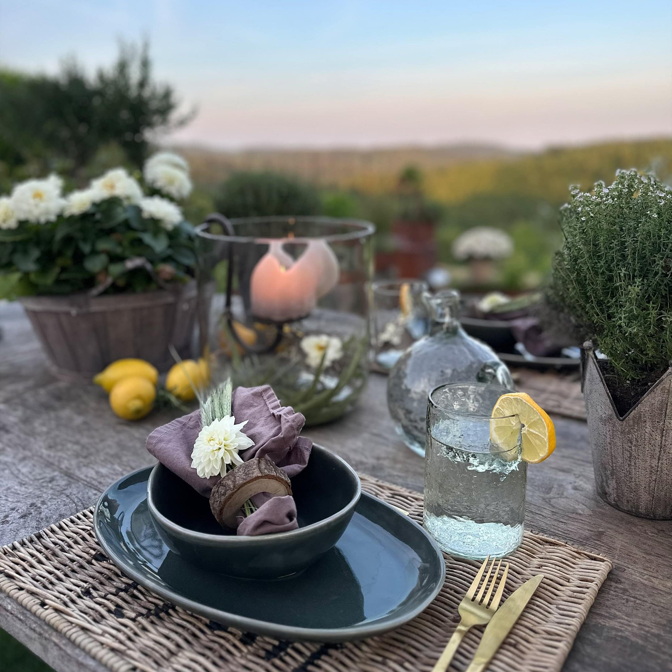 Tavolo rustico con stoviglie in ceramica scura, tovagliolo di lino e bicchiere d'acqua con limone all'aperto