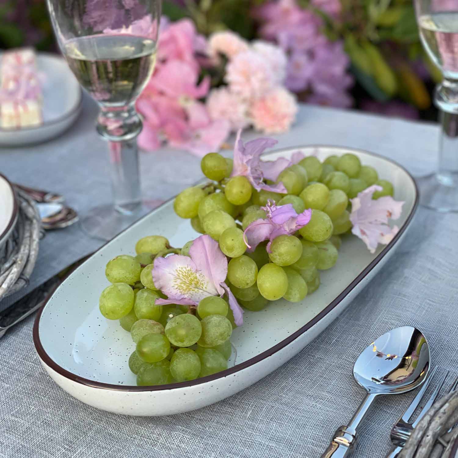 Uva verde con fiori rosa su piatto in ceramica bianca su tovaglia grigia
