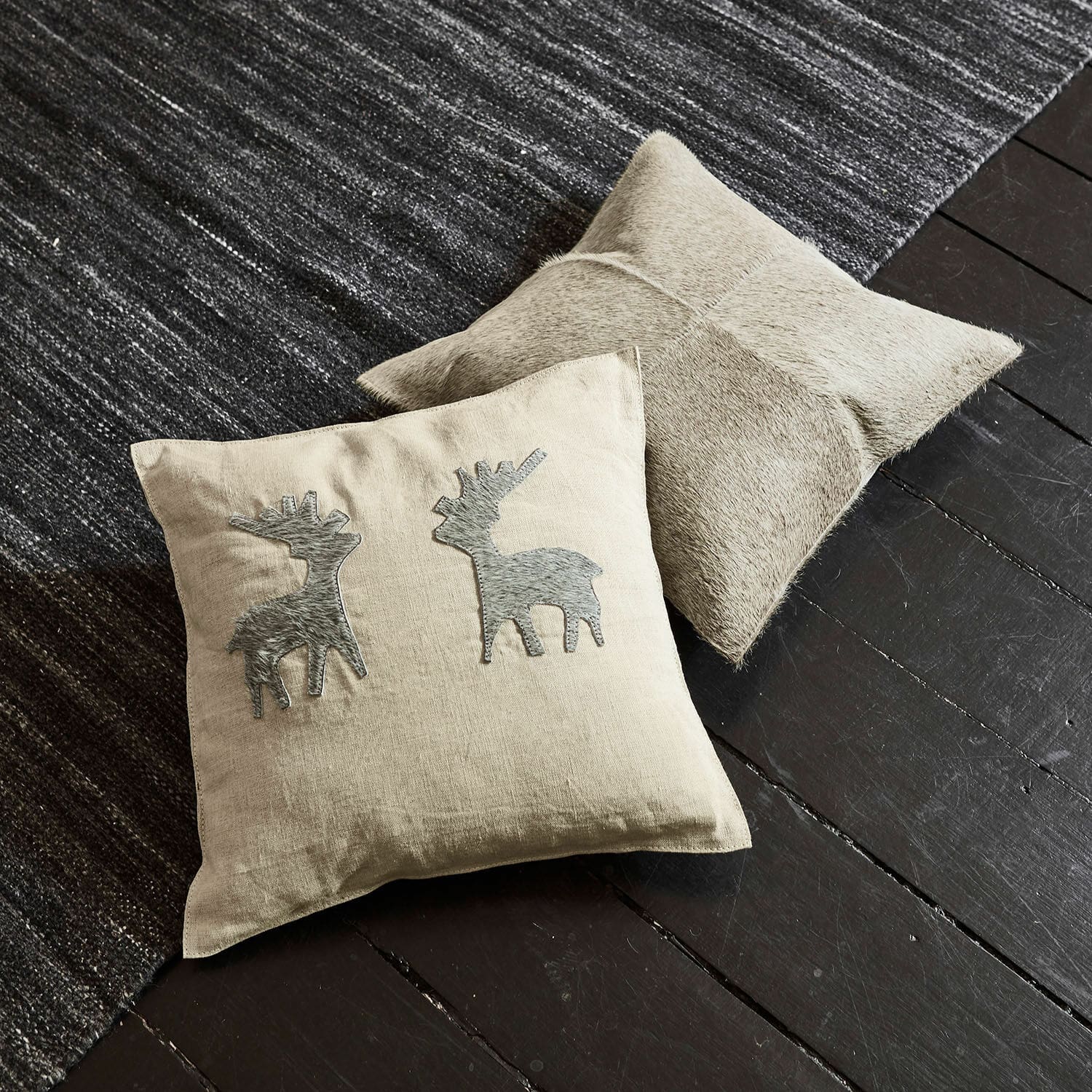 Coppia di copricuscini Beaupuy Cuscino beige in lino con applicazioni di cervi grigi e cuscino in pelle chiara su pavimento scuro e tappeto