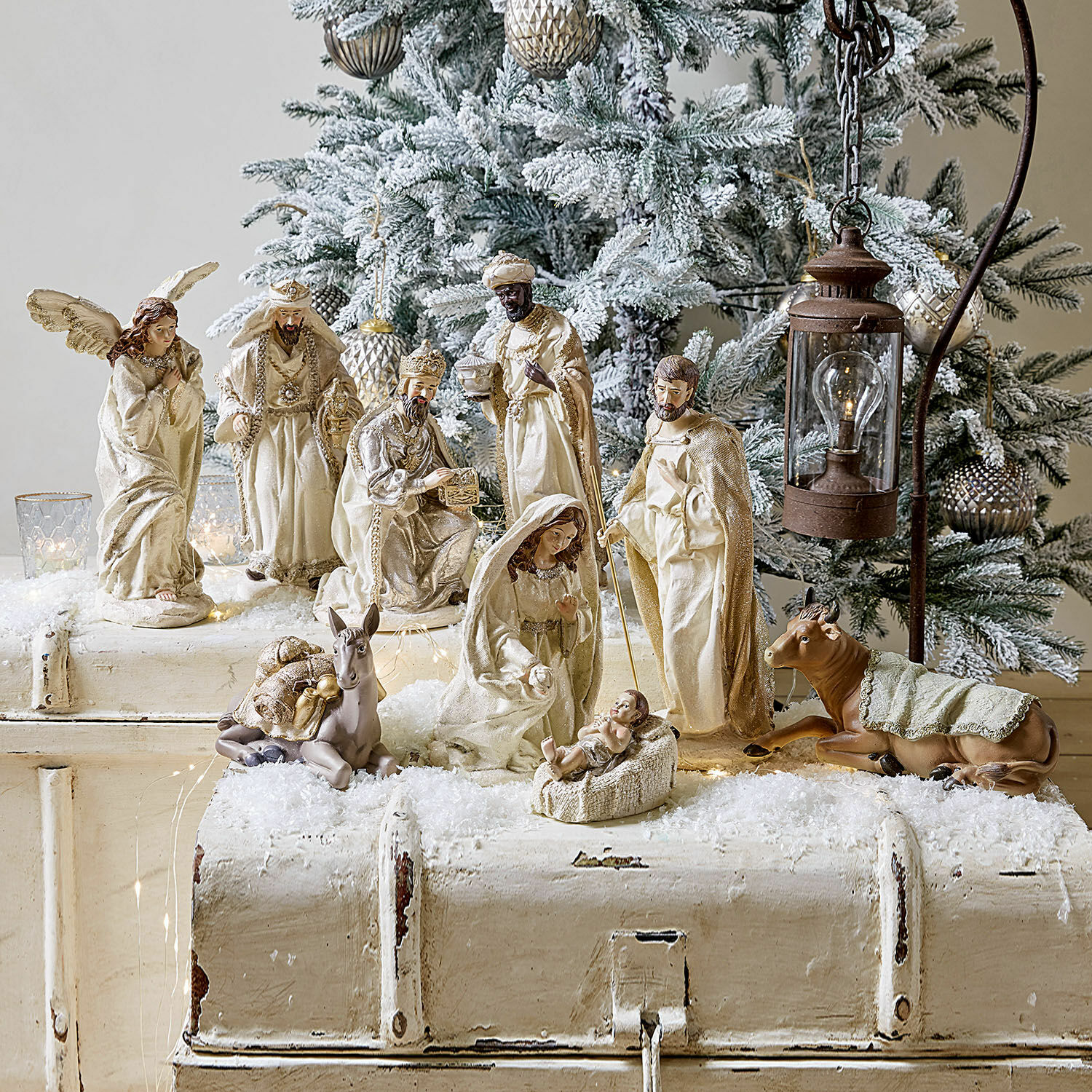 Set di 9 statuine Liré Figure del presepe color crema davanti a un albero di Natale innevato e lanterna rustica